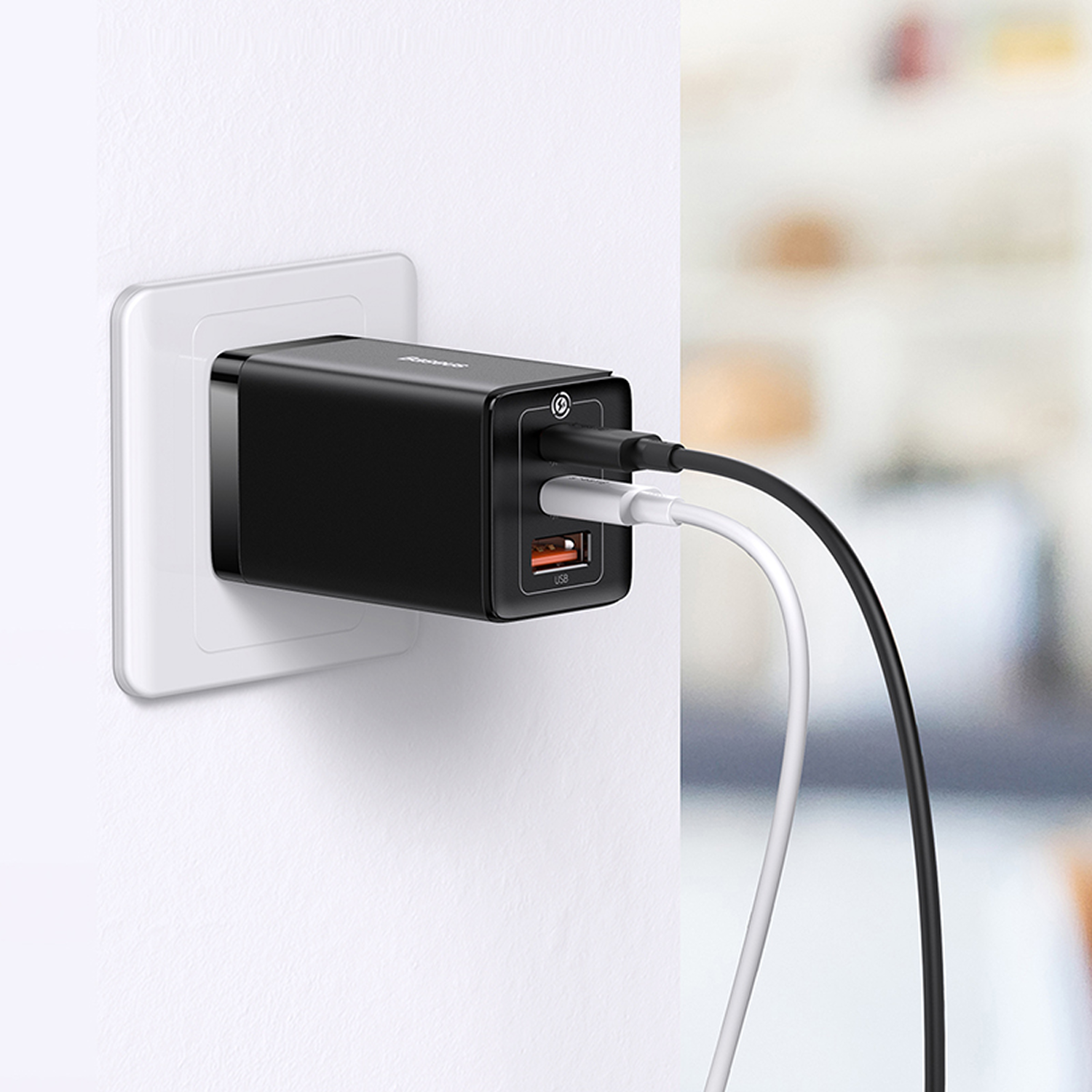 Un cargador negro enchufado a un enchufe de pared blanco. Dos cables, negro y blanco, están conectados al cargador. Fondo borroso.