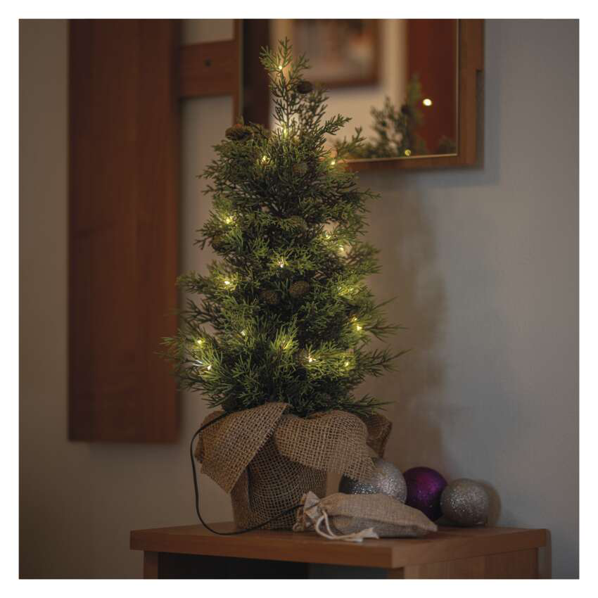 Egy kis karácsonyfa világítással egy faasztalon. Díszek, egy kis táska és egy tükör a háttérben.