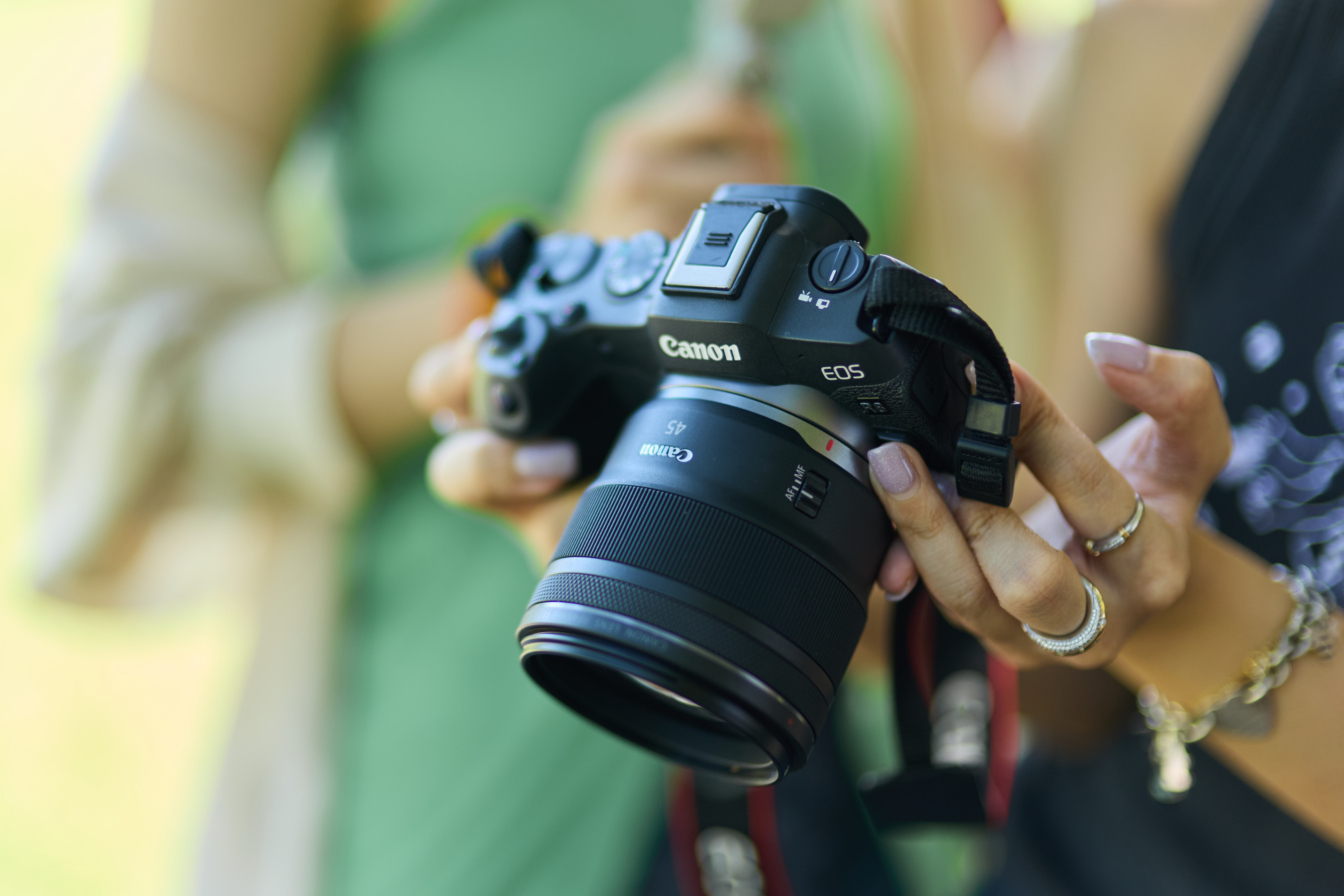Eine Person hält eine Canon EOS-Kamera. Fokus auf Objektiv, Hände und Hintergrund.