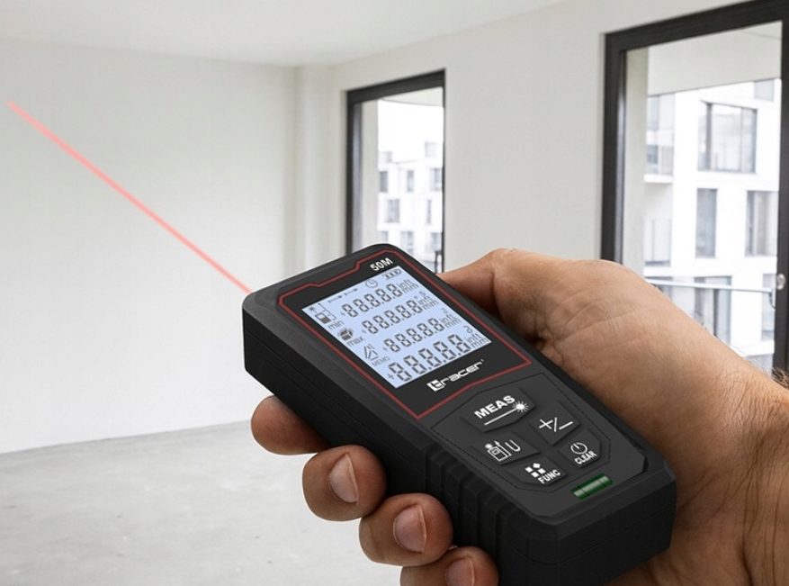 Dłoń trzyma czarny laserowy miernik odległości, emitujący czerwoną wiązkę. Miernik wyświetla liczby. Tło to białe pomieszczenie.