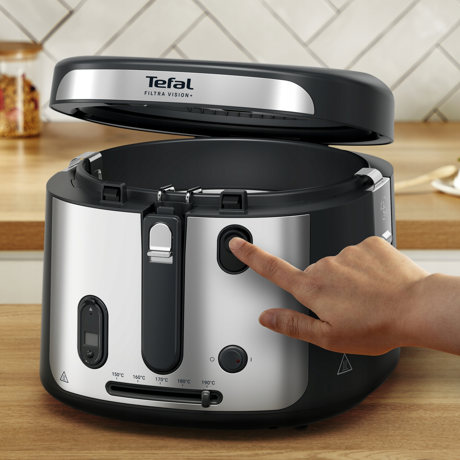 Dłoń naciska przycisk na frytkownicy Tefal. Jest czarna i srebrna, z otwartą pokrywą.