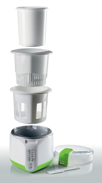 Zdemontowany biało-zielony jogurtownik. Części obejmują pojemnik, wewnętrzne kosze i podstawę z przyciskami. Obecna jest również pokrywa i szpatułka.