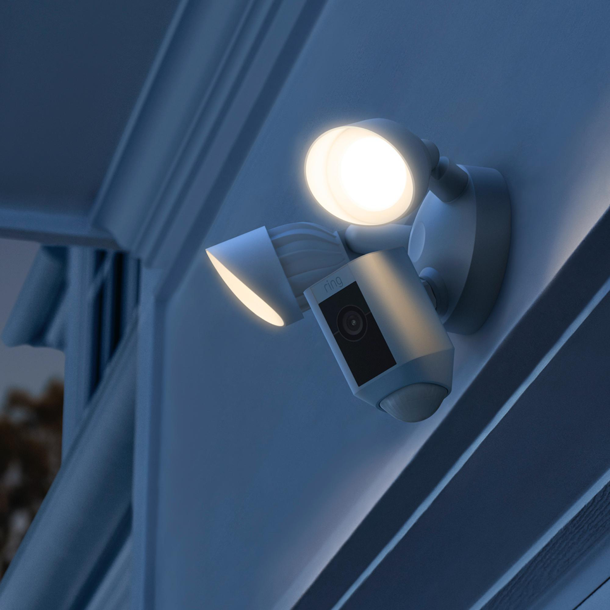 Ring-Flutlichtkamera an einer Wand montiert. Zwei Lichter sind an. Die Szene ist nachts beleuchtet.