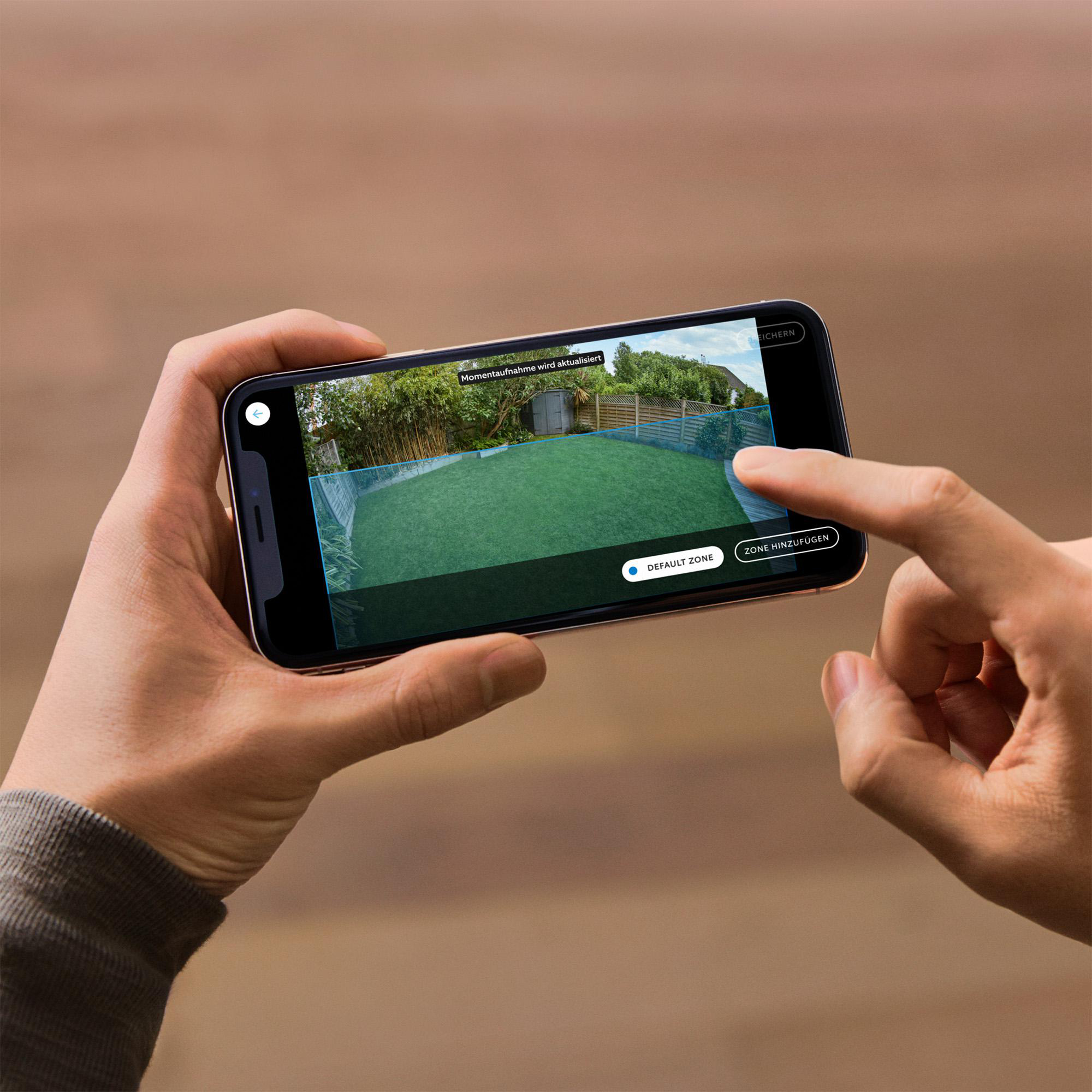 Eine Person hält ein Telefon mit einem grünen Rasen. Das Telefon zeigt einen Garten mit Bäumen und einem Zaun.