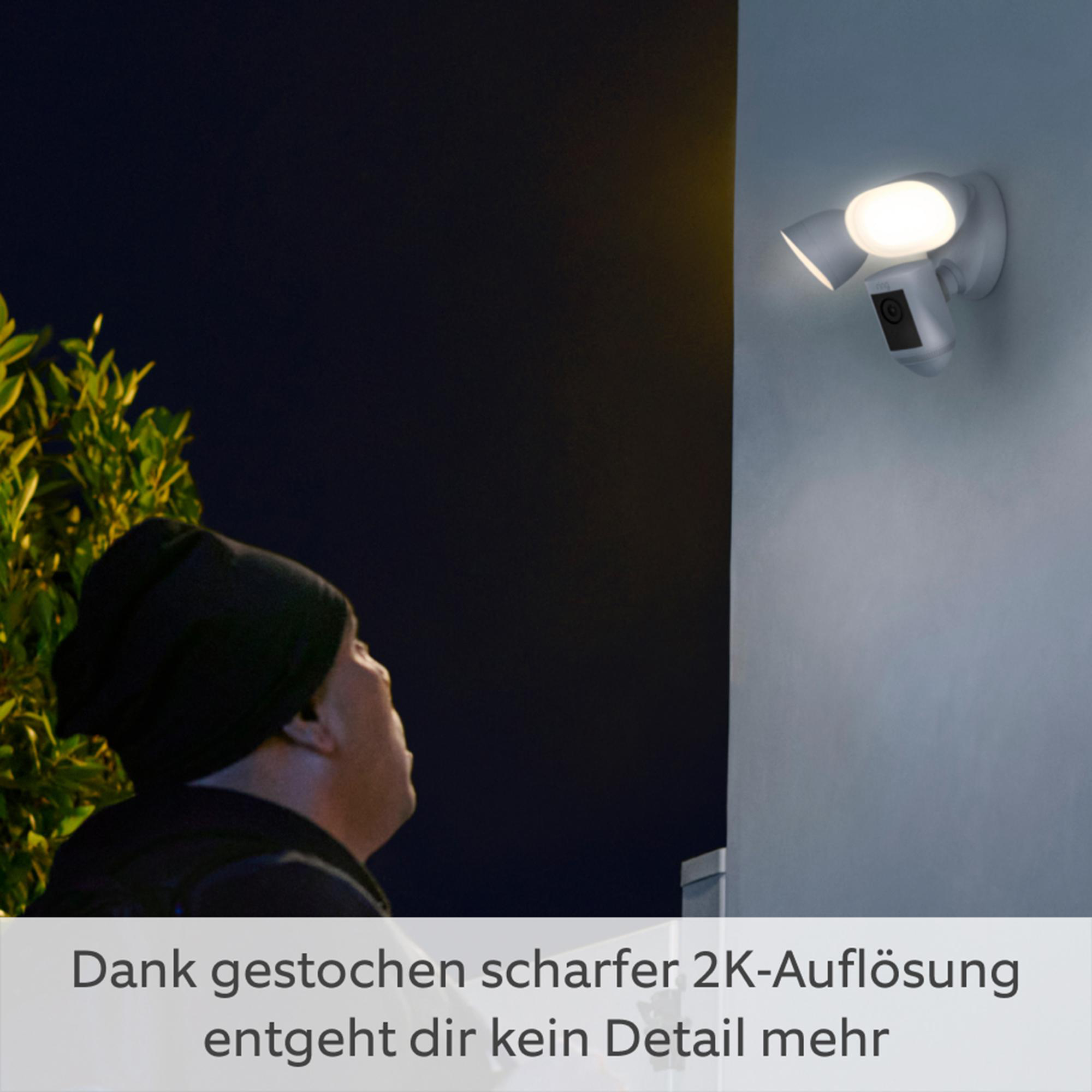 Ein Mann blickt auf eine Sicherheitsleuchte mit Kamera. Dunkler Himmel im Hintergrund.