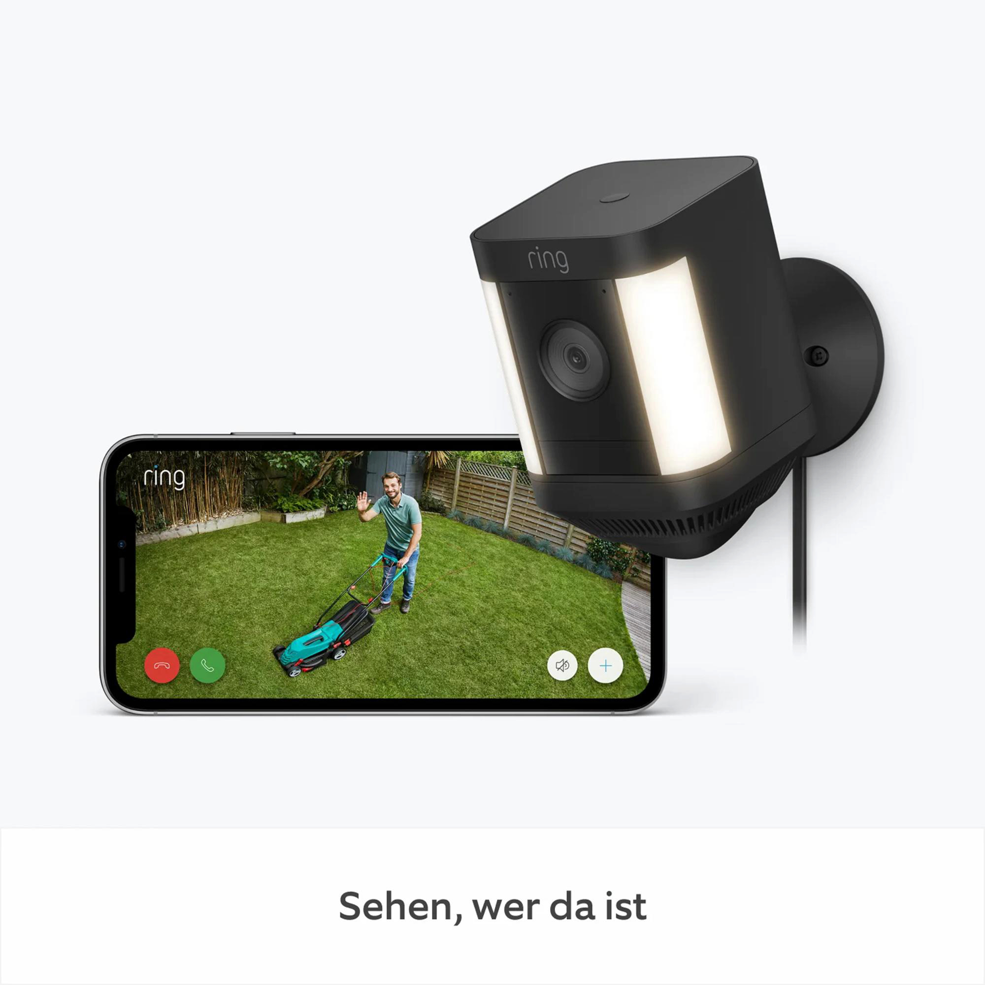 Eine Ring-Sicherheitskamera zeigt einen Mann, der den Rasen mäht. Die Kamera ist neben einem Smartphone-Bildschirm montiert.