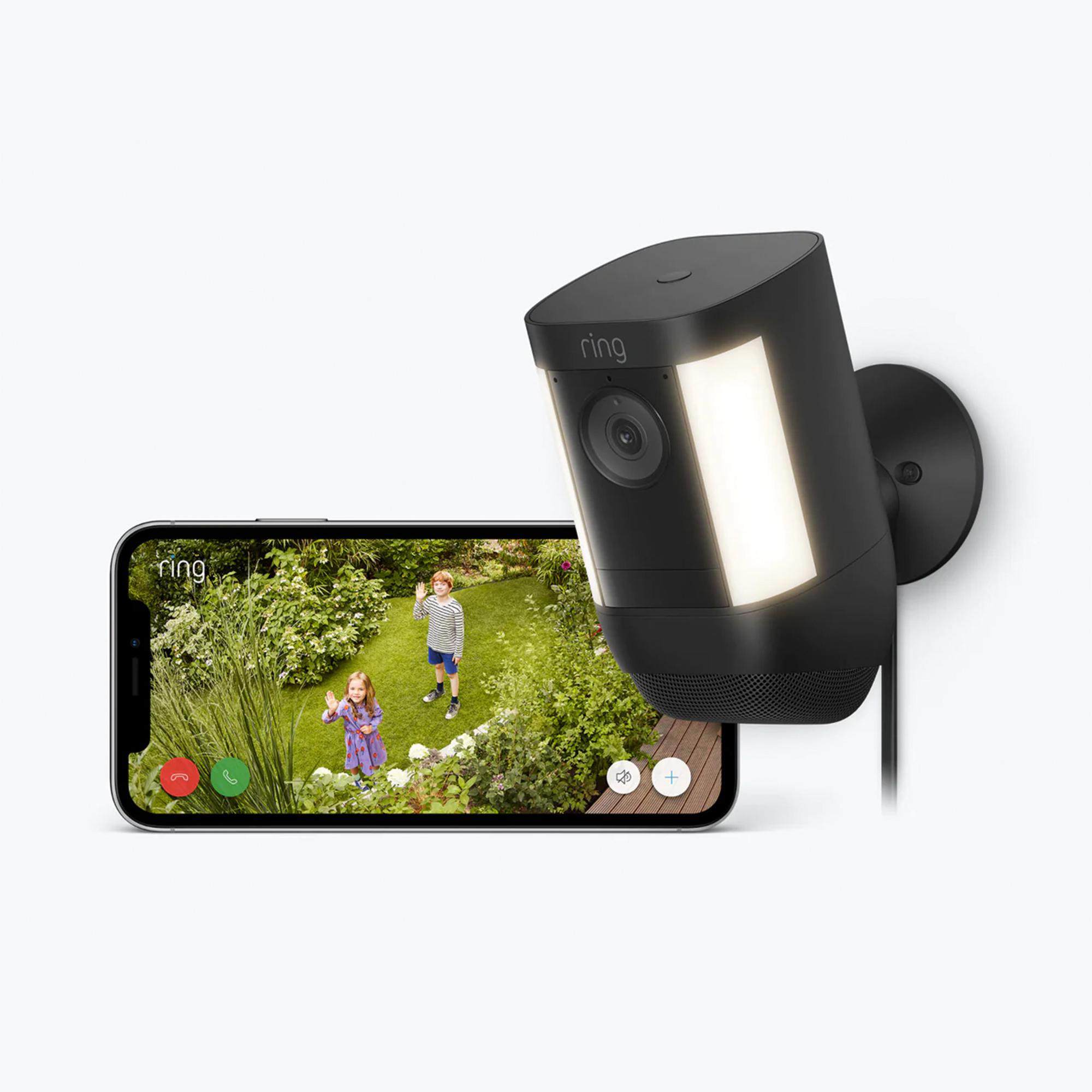 Ring-Sicherheitskamera und Telefonbildschirm, auf dem zwei Kinder in einem Garten zu sehen sind. Kamera hat Licht an.