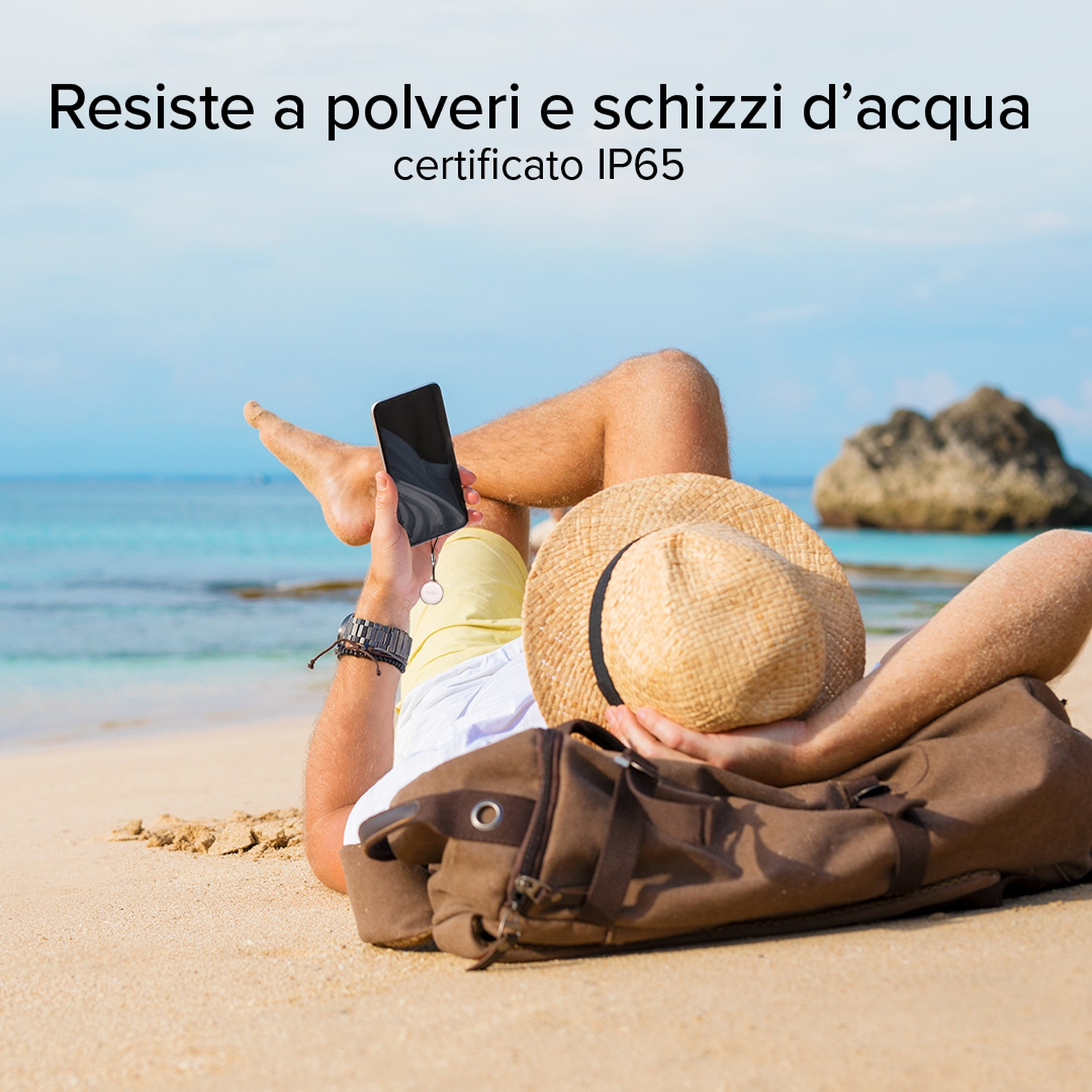 Uomo sulla spiaggia con telefono. Indossa orologio e cappello. Borsa marrone sulla sabbia. Mare e cielo sullo sfondo.