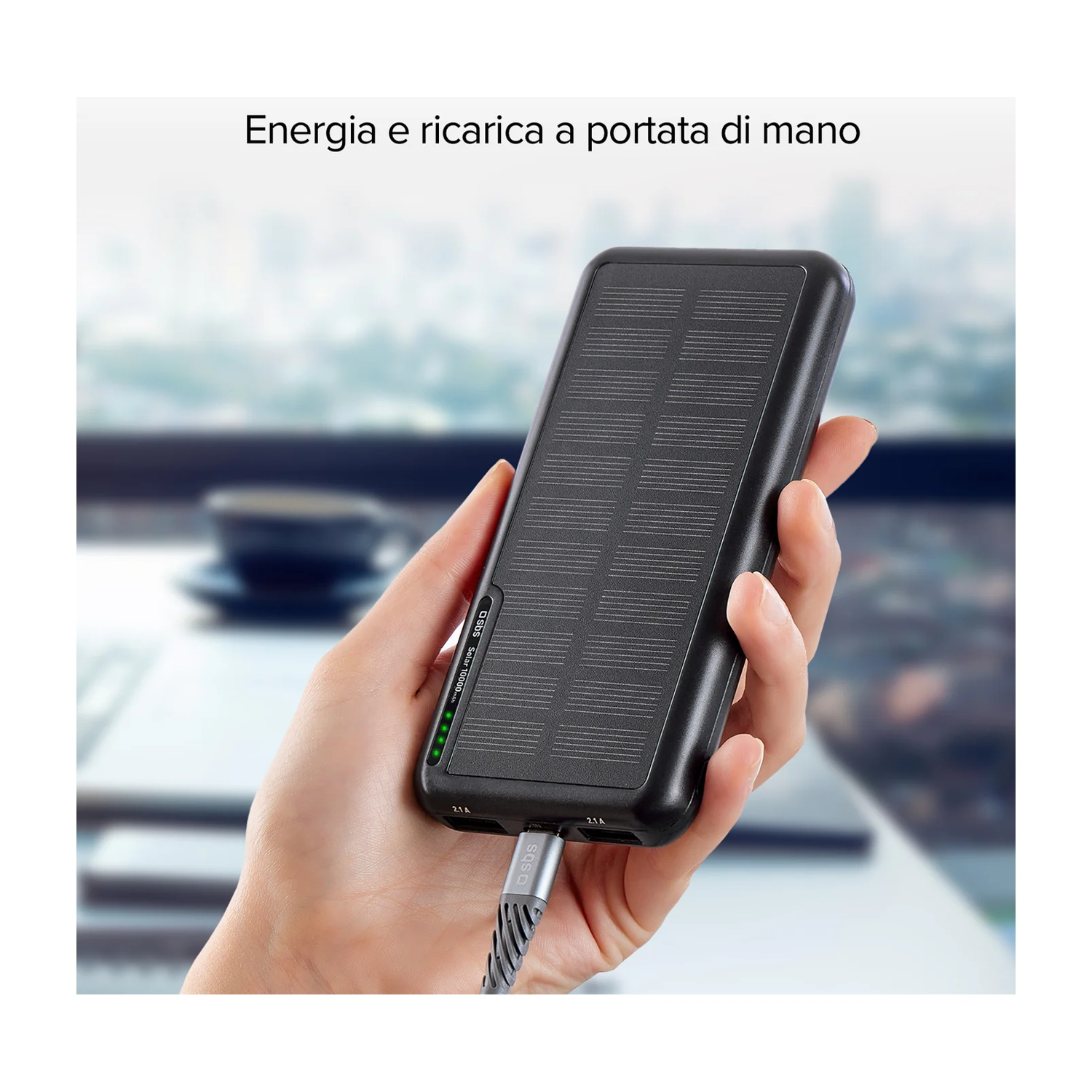 Una mano tiene un power bank solare nero con un cavo di ricarica argentato collegato. Il power bank mostra lo stato di carica.