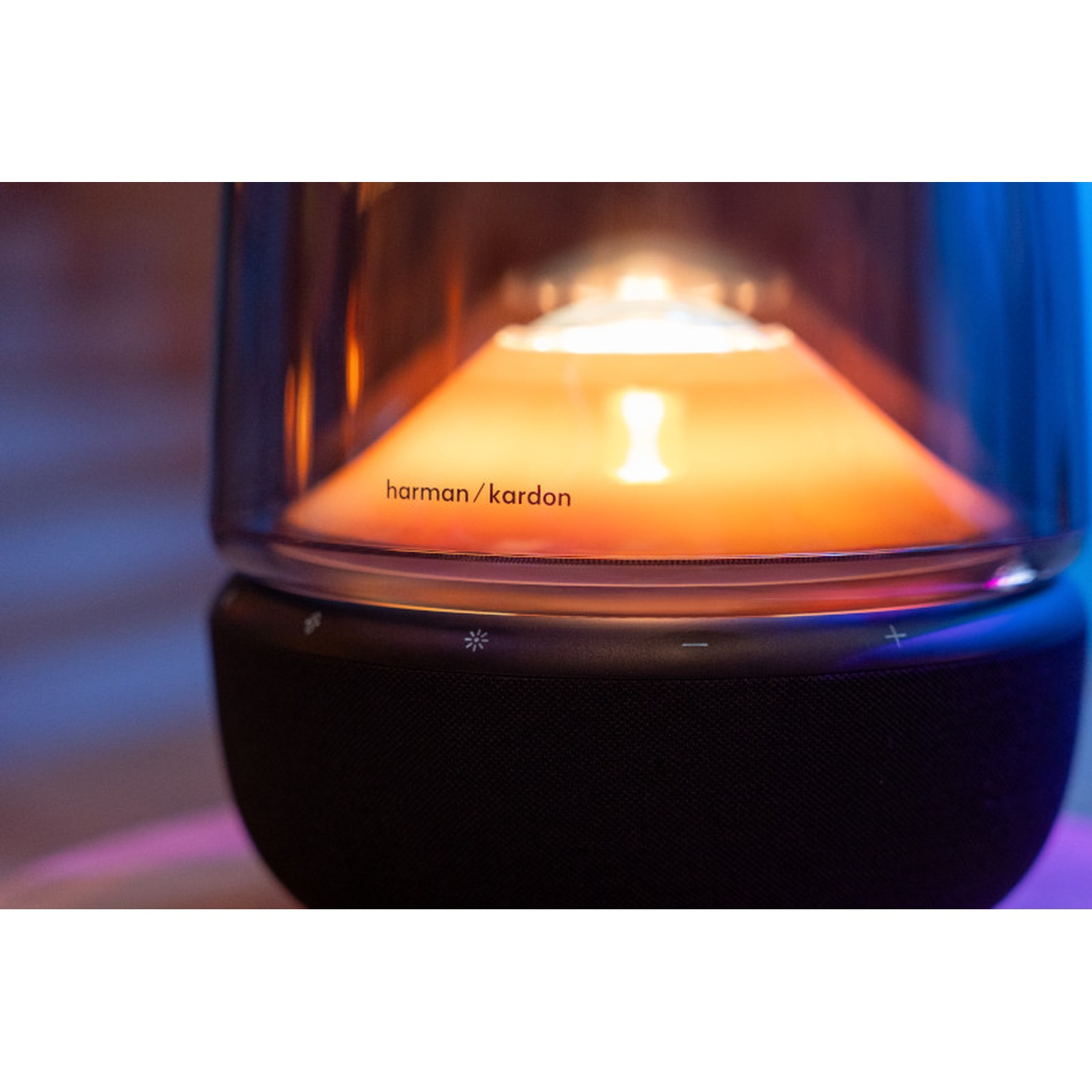 Un primo piano di un altoparlante nero con la parte superiore in vetro. La parte superiore ha un bagliore arancione con le parole 'harman/kardon'.