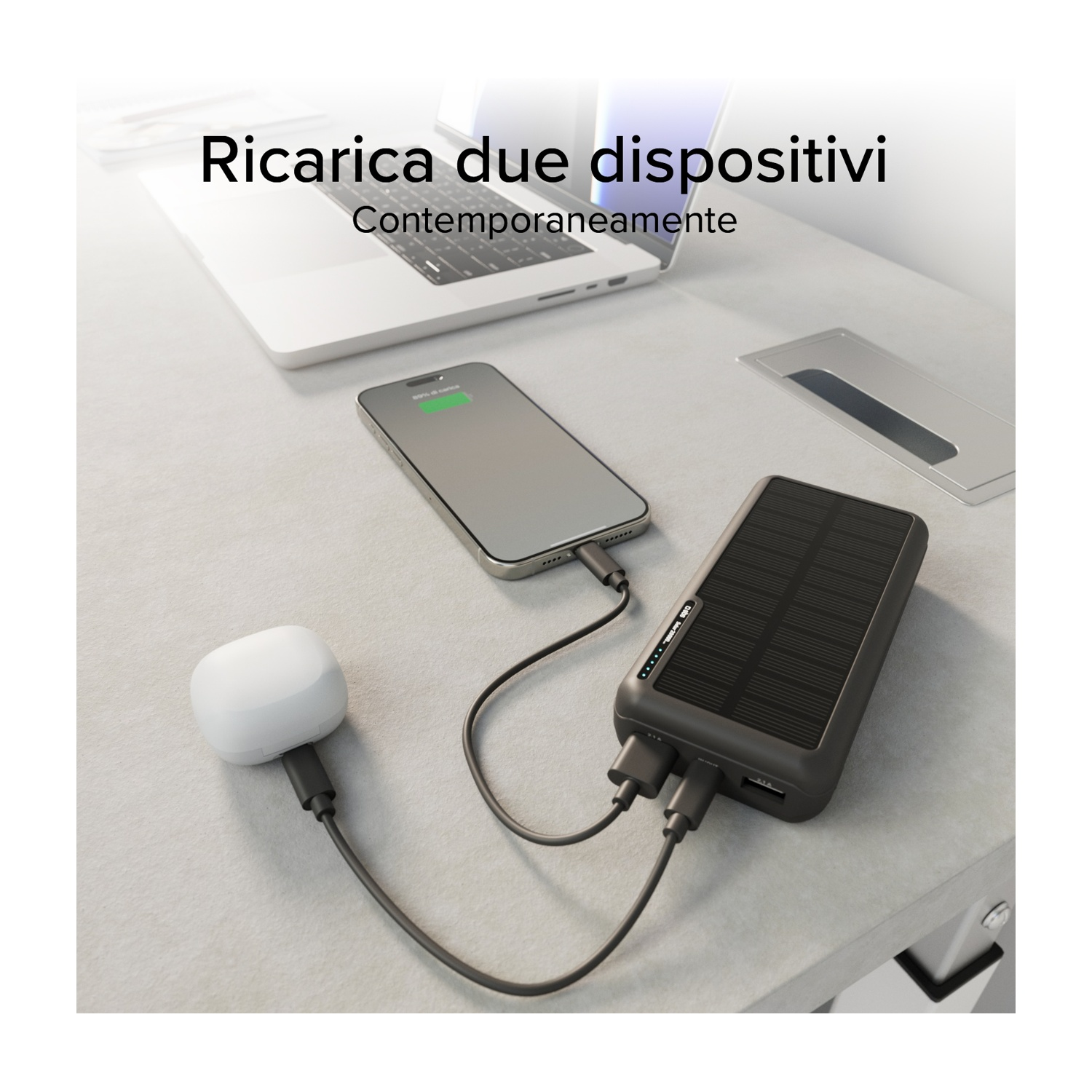 Un telefono e un dispositivo bianco si caricano da un power bank solare nero su una scrivania, vicino a un laptop.