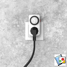 Eine weiße Steckdose mit eingestecktem schwarzen Stecker und einem Timer an einer grau strukturierten Wand.