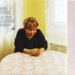 Frau mit kurzen Haaren sitzt an einem Tisch mit geblümter Tischdecke. Text: Mavis Staples, Sad and Beautiful World.