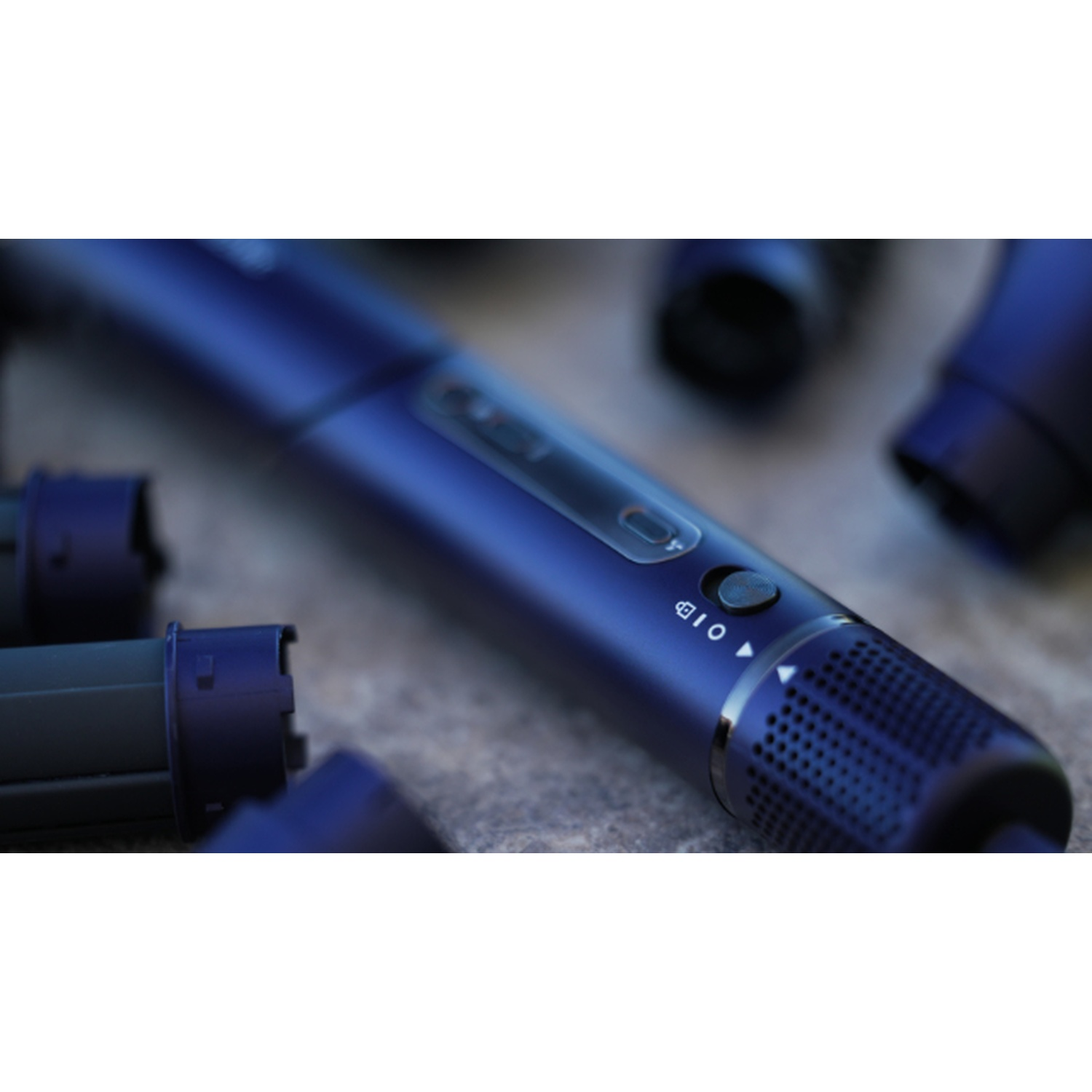 Primo piano di un dispositivo blu scuro con un pulsante e piccoli fori. Altre parti blu scuro sullo sfondo sfocato.