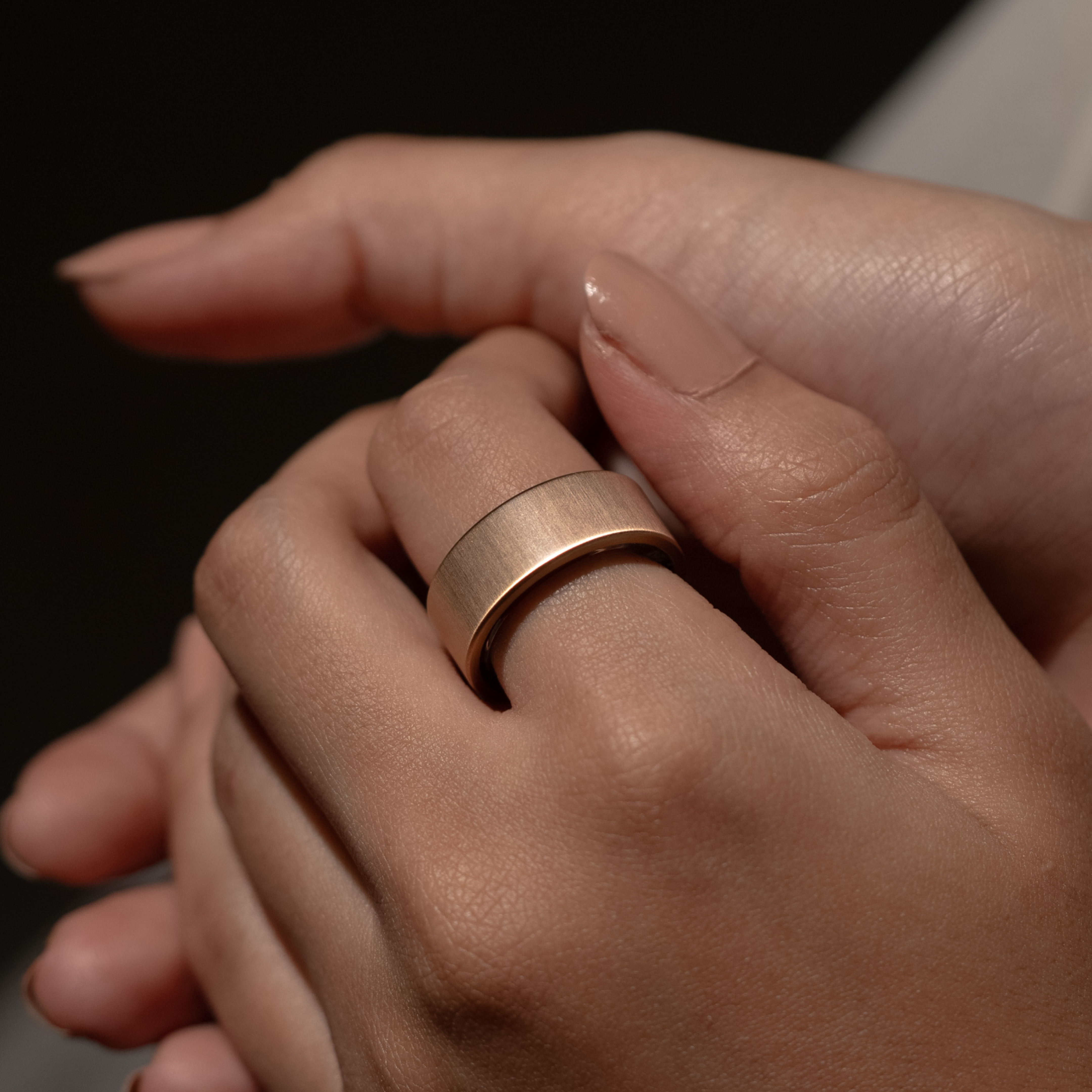 Eine Hand hält eine andere und zeigt einen goldenen Ring an einem Finger. Der Ring ist dick und glatt.