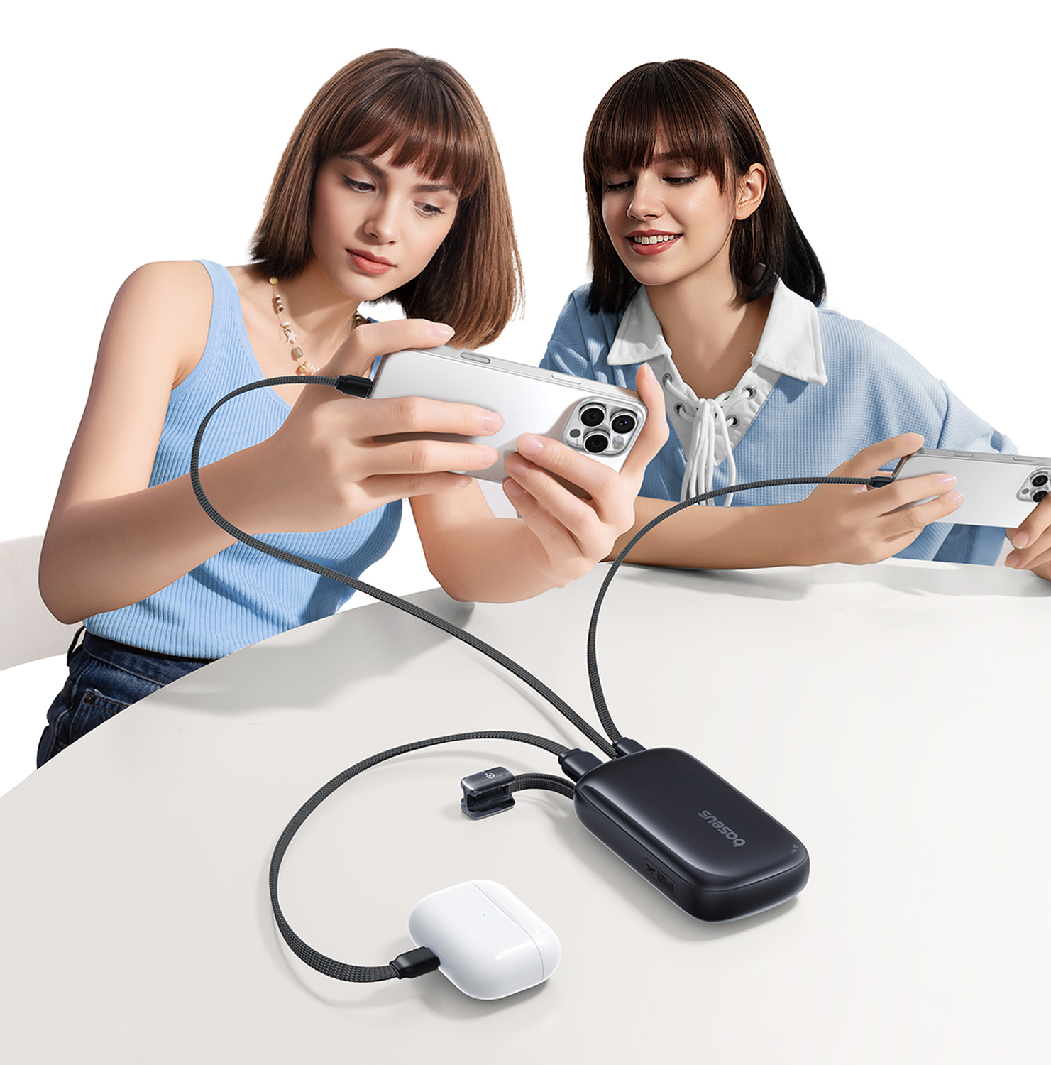 Dos mujeres sostienen teléfonos conectados a un cargador negro. Un estuche Airpod y un cable de carga también son visibles en una mesa blanca.