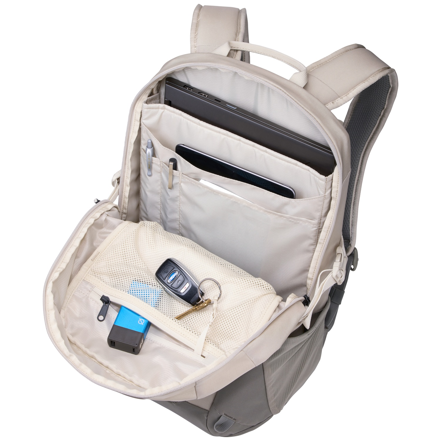 Open rugzak met laptop, tablet, pennen, sleutels en een powerbank. Beige en grijze kleuren domineren het ontwerp, tonen de inhoud.