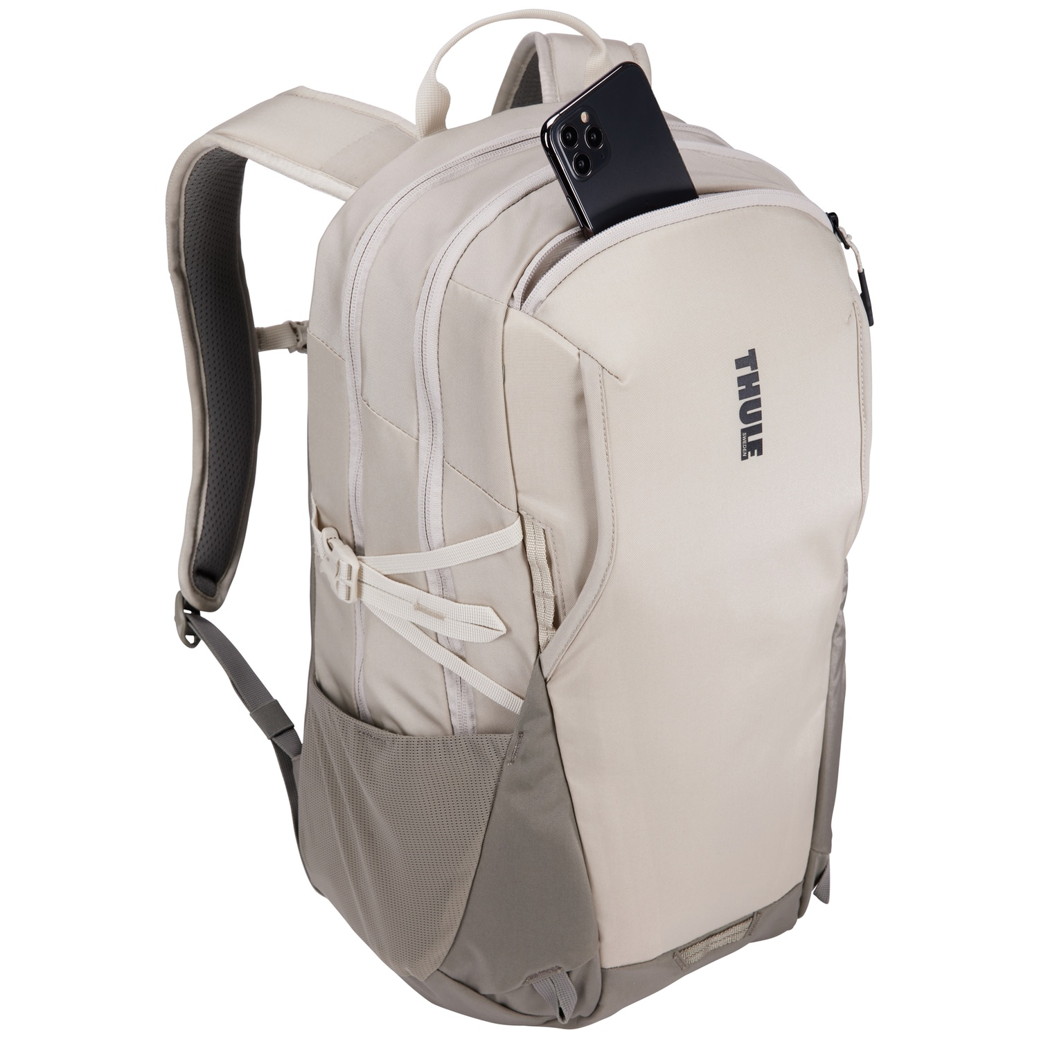 Een beige Thule-rugzak met een zwarte telefoon in de bovenzak, riemen en een handvat. Grijze en beige kleuren.