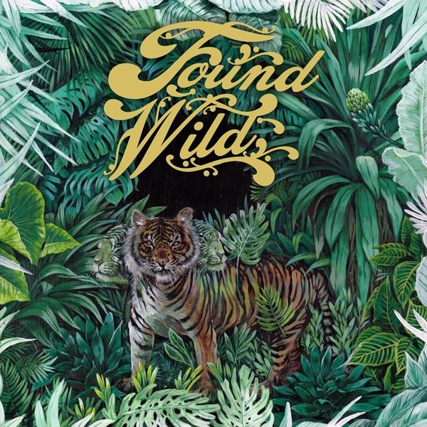 Ein Tiger steht inmitten üppigen grünen Laubes. Der Text „Found Wilds“ ist in Gold gehalten. Das Kunstwerk zeigt eine lebendige Dschungelszene.