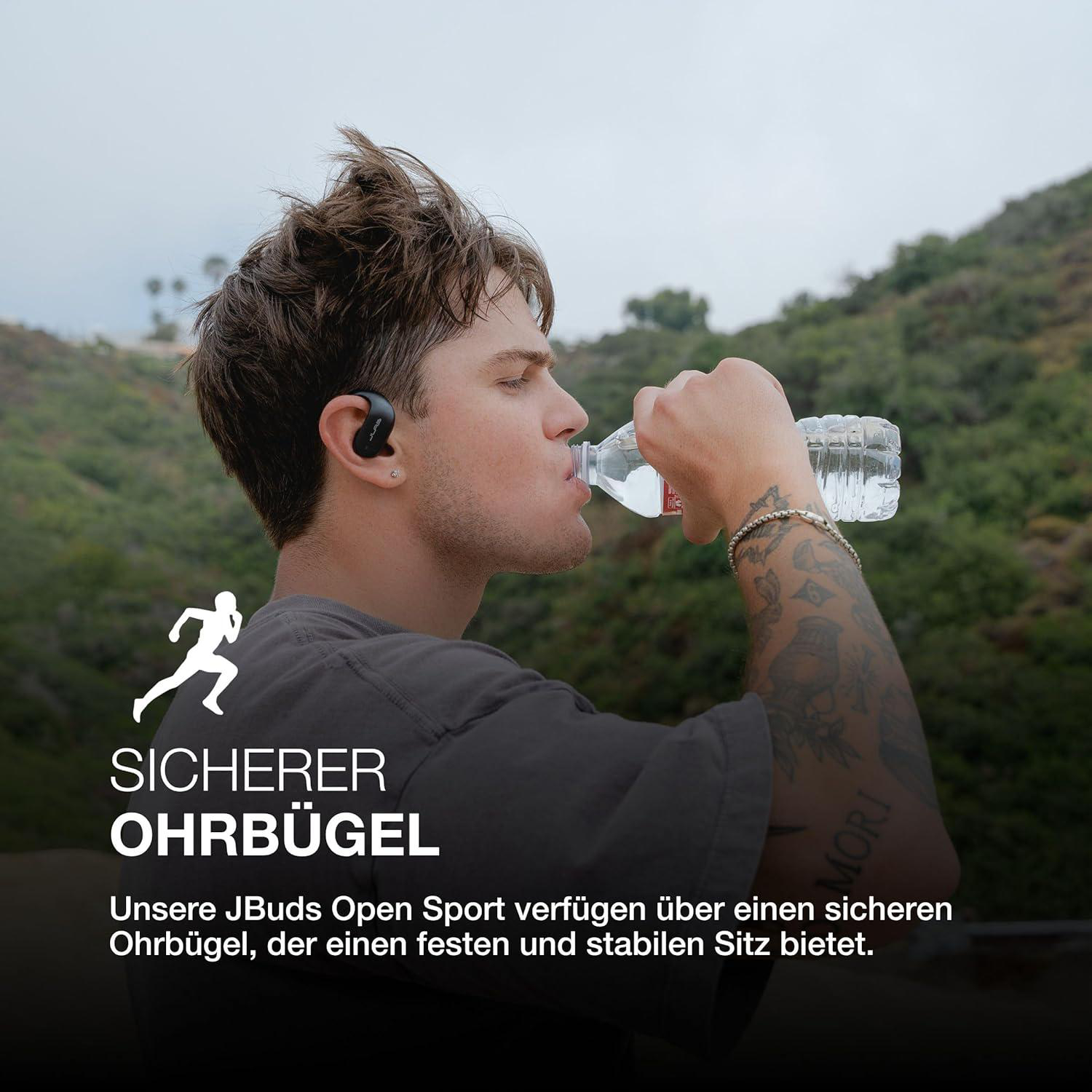 Ein Mann trinkt Wasser aus einer Flasche. Er trägt Ohrhörer und hat Tätowierungen. Der Hintergrund zeigt Grün.
