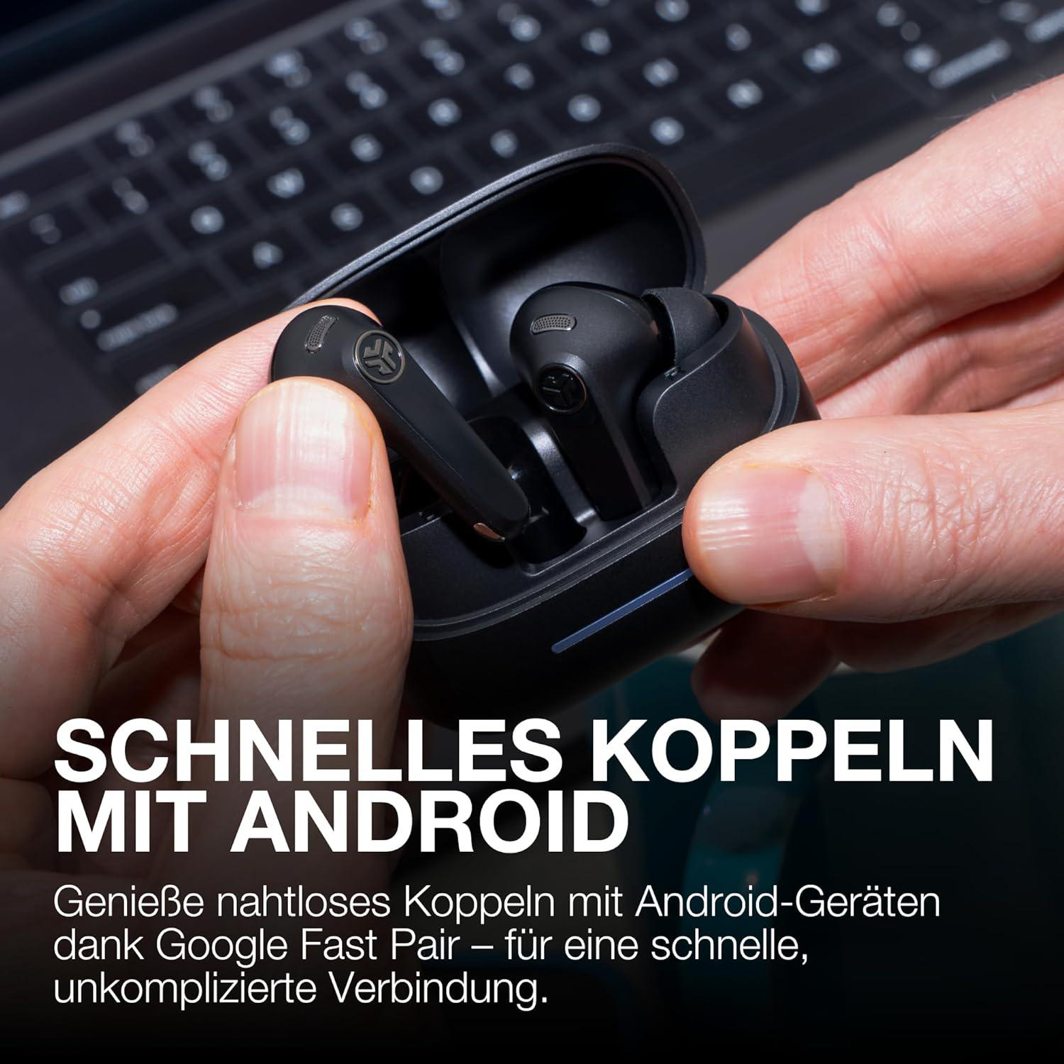 Hände halten schwarze kabellose Ohrhörer in einem Ladeetui. Eine Laptop-Tastatur ist im Hintergrund. Text lautet: SCHNELLES KOPPELN MIT ANDROID.