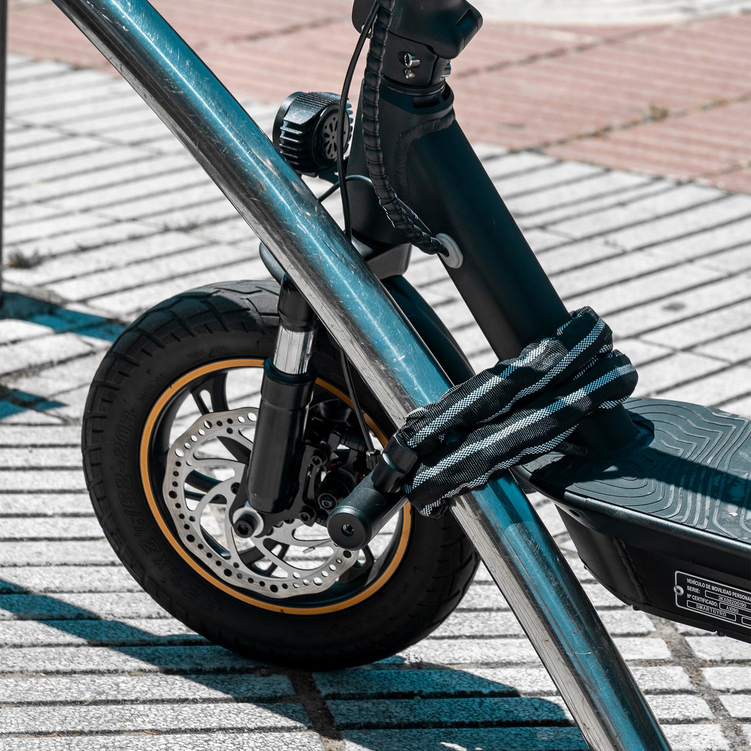 Primer plano de una rueda de patinete eléctrico, asegurada a una barra de metal con una cadena. El patinete está sobre ladrillos.