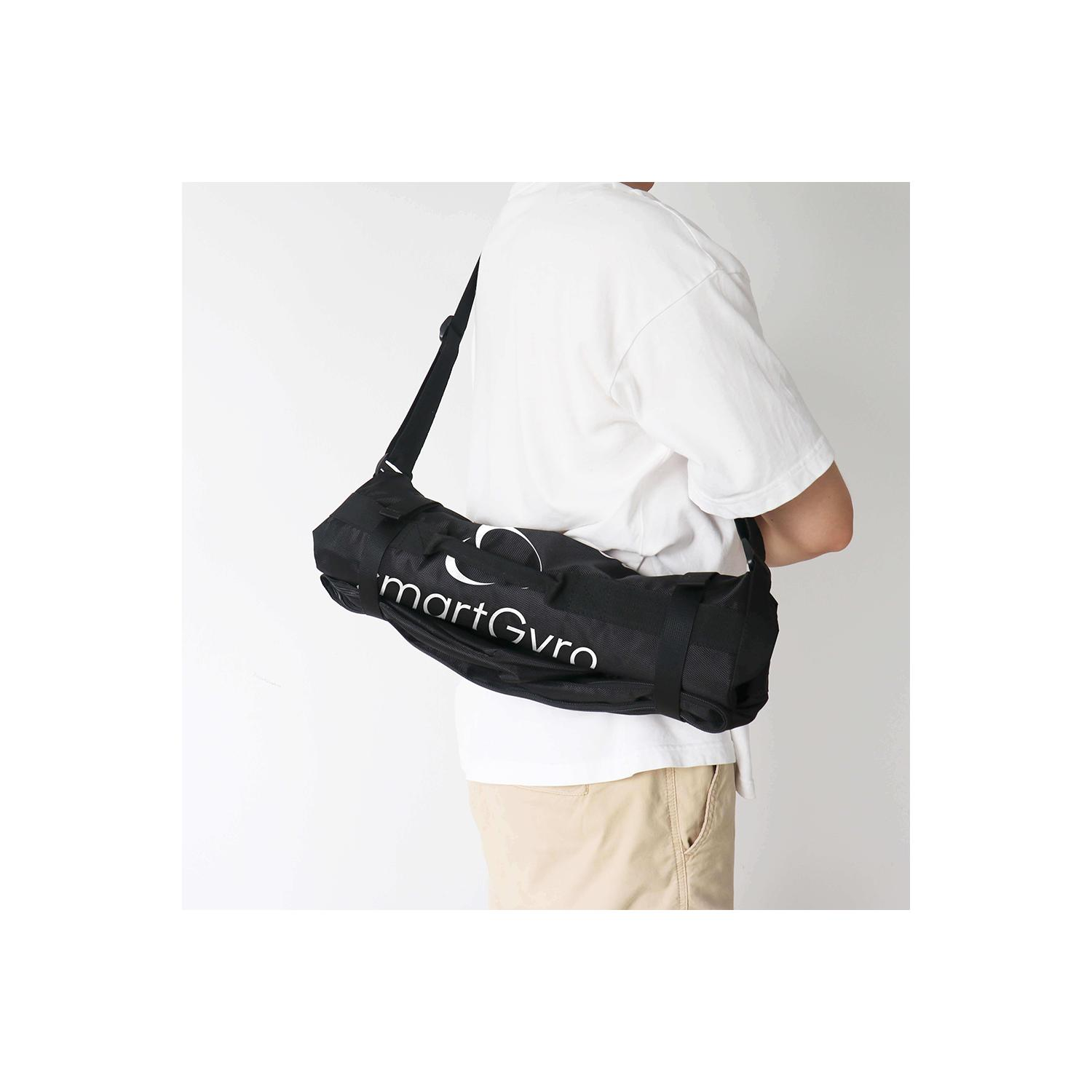 Una persona con camisa blanca y pantalones caqui lleva una bolsa negra con el texto 'martGyro' sobre el hombro.