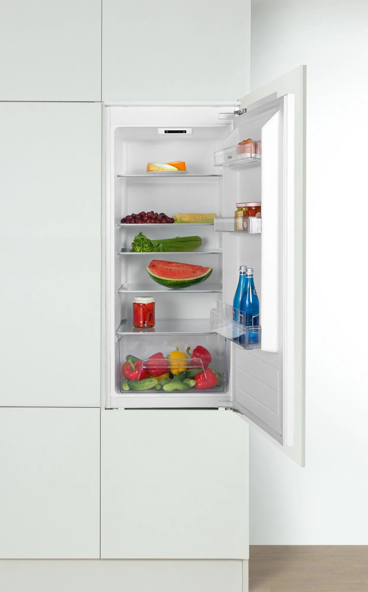 Otwarta lodówka wypełniona owocami i warzywami, w tym arbuzem, papryką, ogórkami i winogronami.