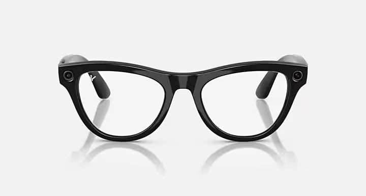 Czarne okulary Ray-Ban z przezroczystymi soczewkami, odbijające się na białej powierzchni. Okulary mają grubą oprawkę i wbudowane kamery.