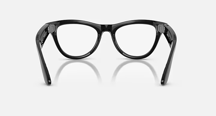 Czarne okulary z przezroczystymi szkłami skierowane lekko w górę. Oprawki odbijają się na białej powierzchni.
