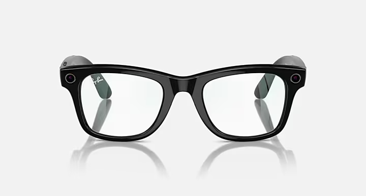 Czarne okulary Ray-Ban ze szkłami i kamerami na oprawkach, odbijające się na białej powierzchni.