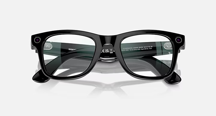 Czarne okulary Ray-Ban na białej powierzchni. Okulary mają przezroczyste soczewki, dwie kamery i mały przycisk na każdym zausznika.