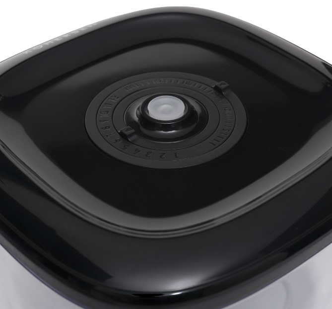 Zbliżenie czarnej pokrywy pojemnika. Centralny cyferblat ma cyfry i przezroczysty plastikowy guzik. Pokrywa jest błyszcząca i odbijająca światło.