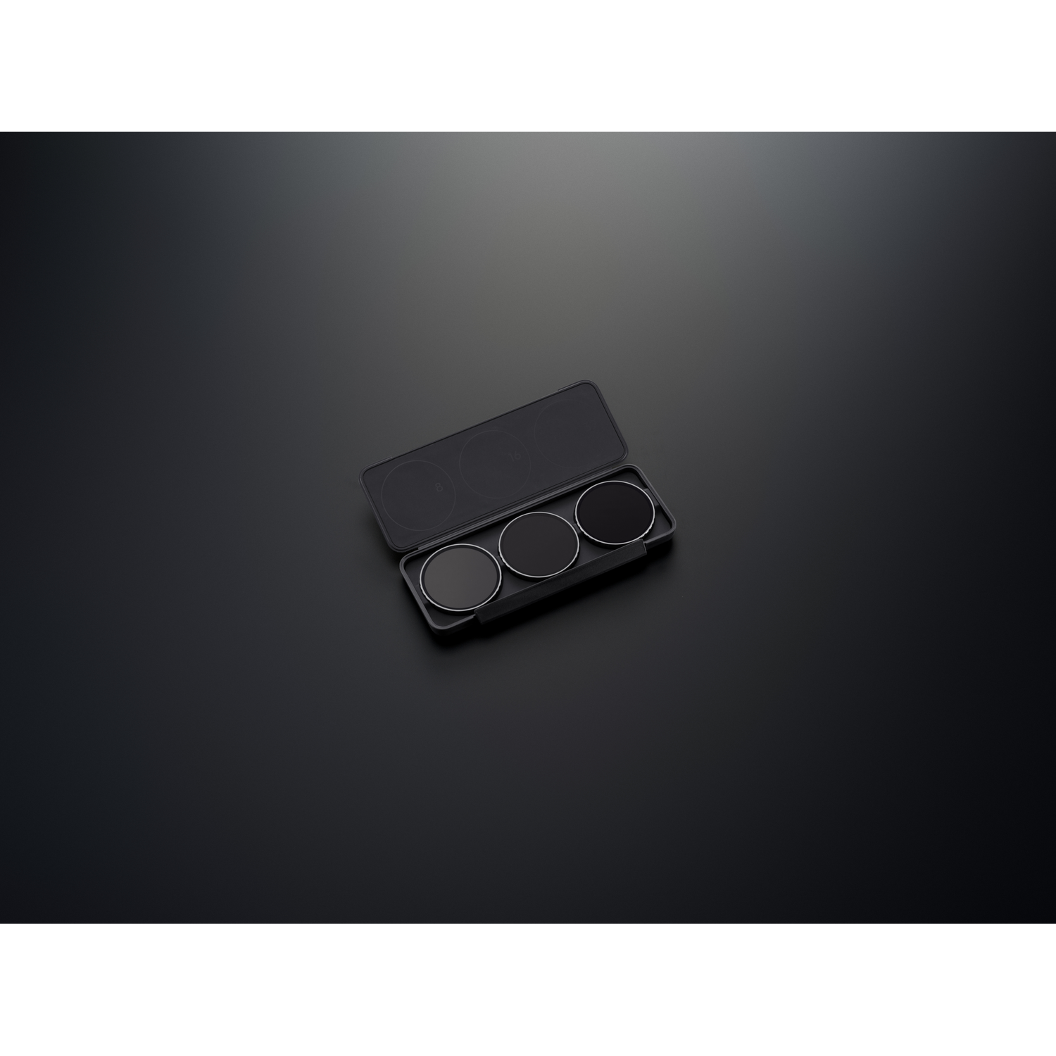 Drie cirkelvormige camerafilters in een zwarte etui op een zwart oppervlak. De filters zijn verschillend donker.