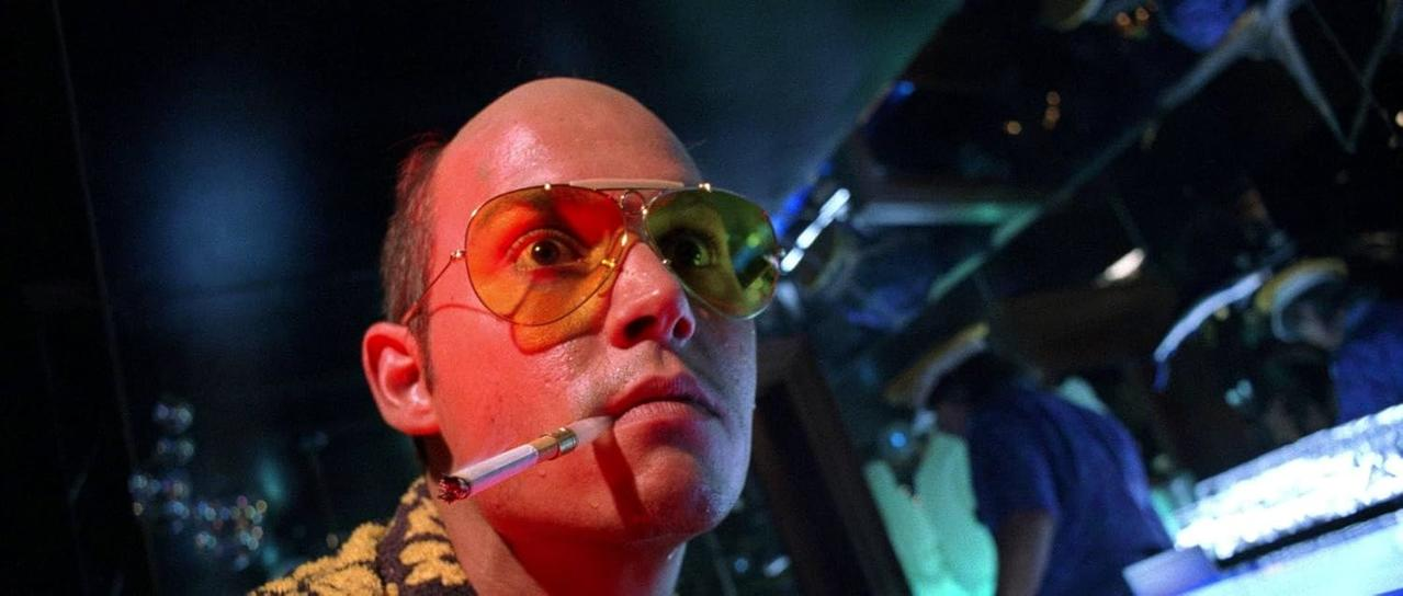 Mann mit gelber Sonnenbrille raucht eine Zigarette. Rote Beleuchtung. Der Hintergrund ist verschwommen.