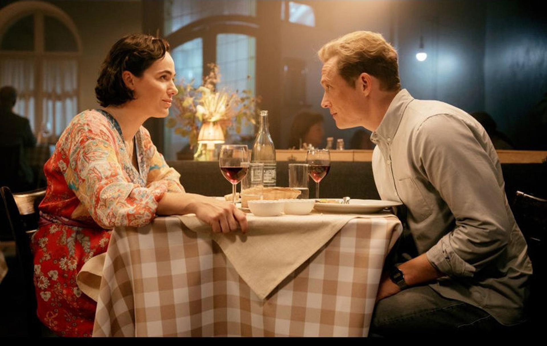 Ein Mann und eine Frau sitzen sich an einem Tisch gegenüber, Weingläser vorhanden. Restaurant-Setting mit warmer Atmosphäre.