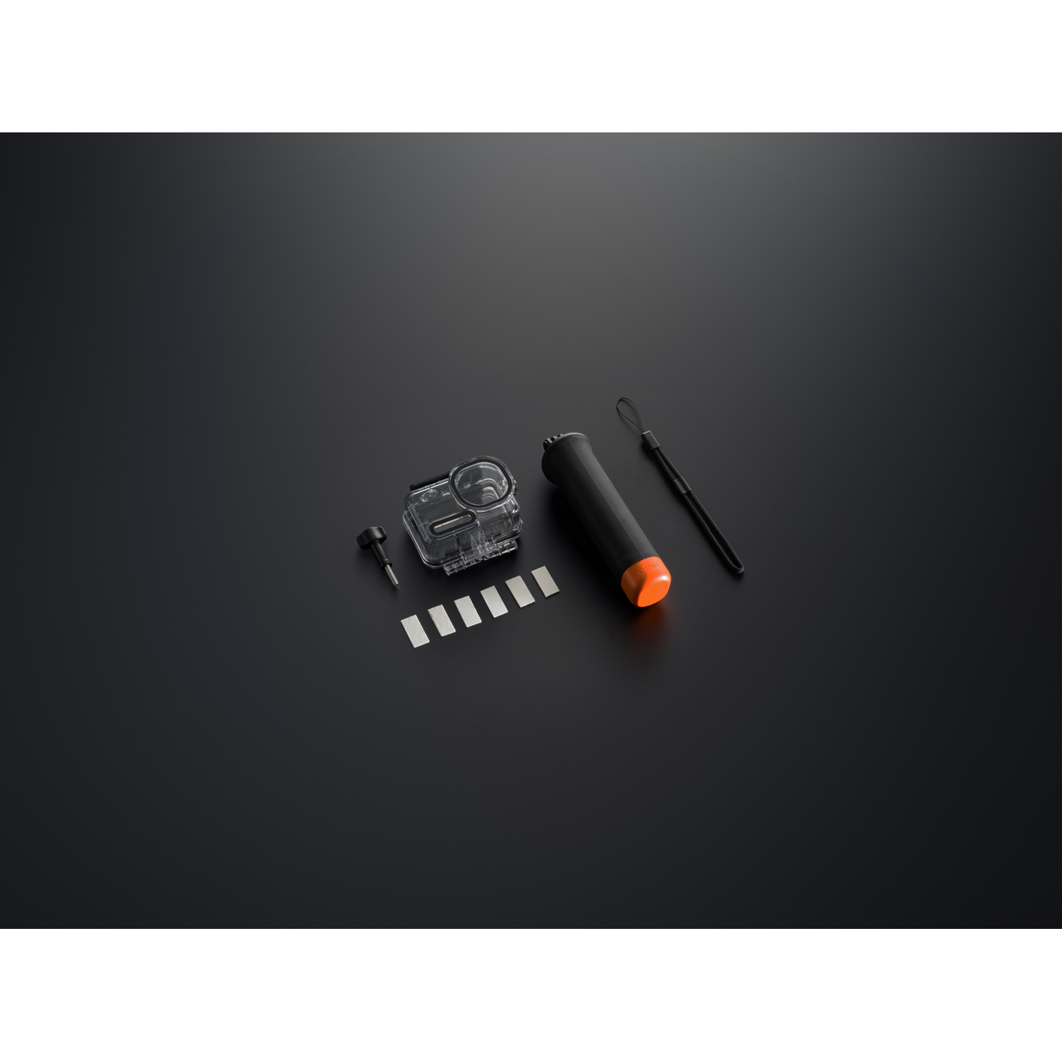 Een actiecamera kit is uitgestald op een zwart oppervlak. Het bevat een doorzichtige waterdichte behuizing, een zwarte handgreep met een oranje uiteinde en metalen lipjes.