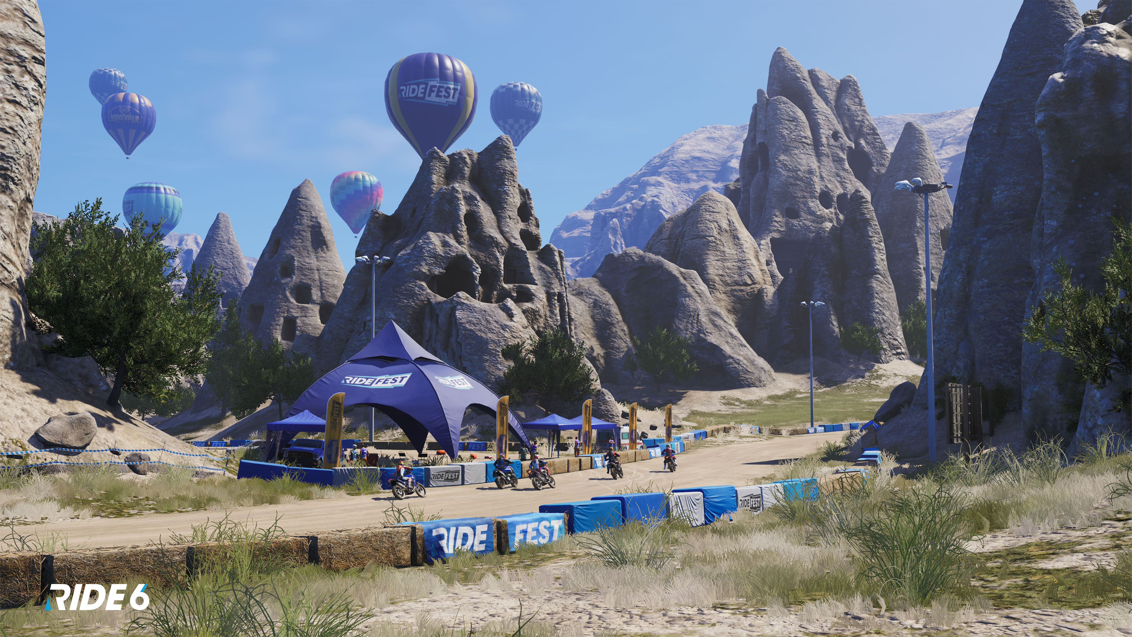 Heißluftballons über einer Rennstrecke mit Motorrädern. Felsformationen und ein blaues Zelt mit 'Ride Fest' sind sichtbar.