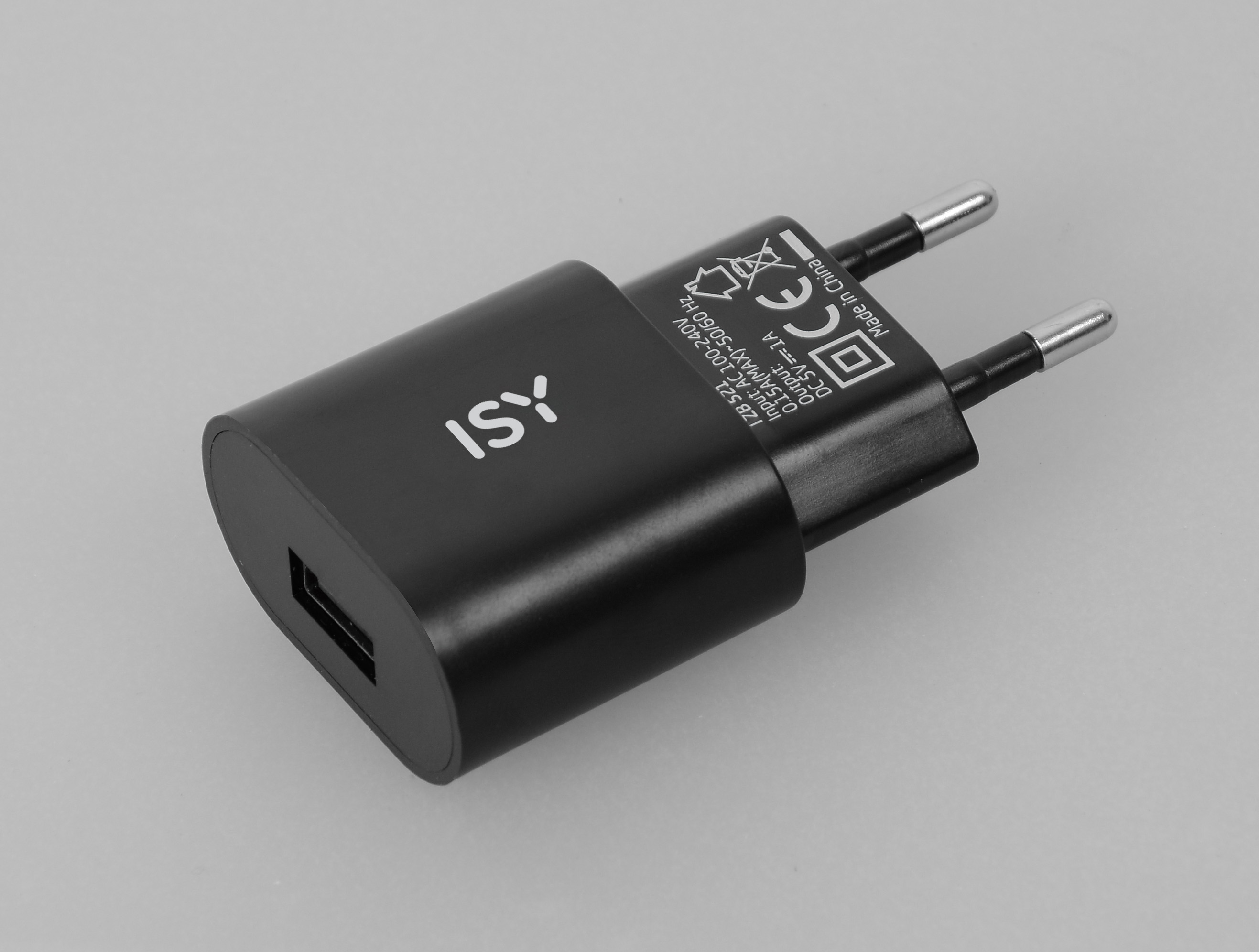 Ein schwarzes ISY USB-Ladegerät auf grauem Untergrund. Es hat Stecker, einen USB-Anschluss und Text.