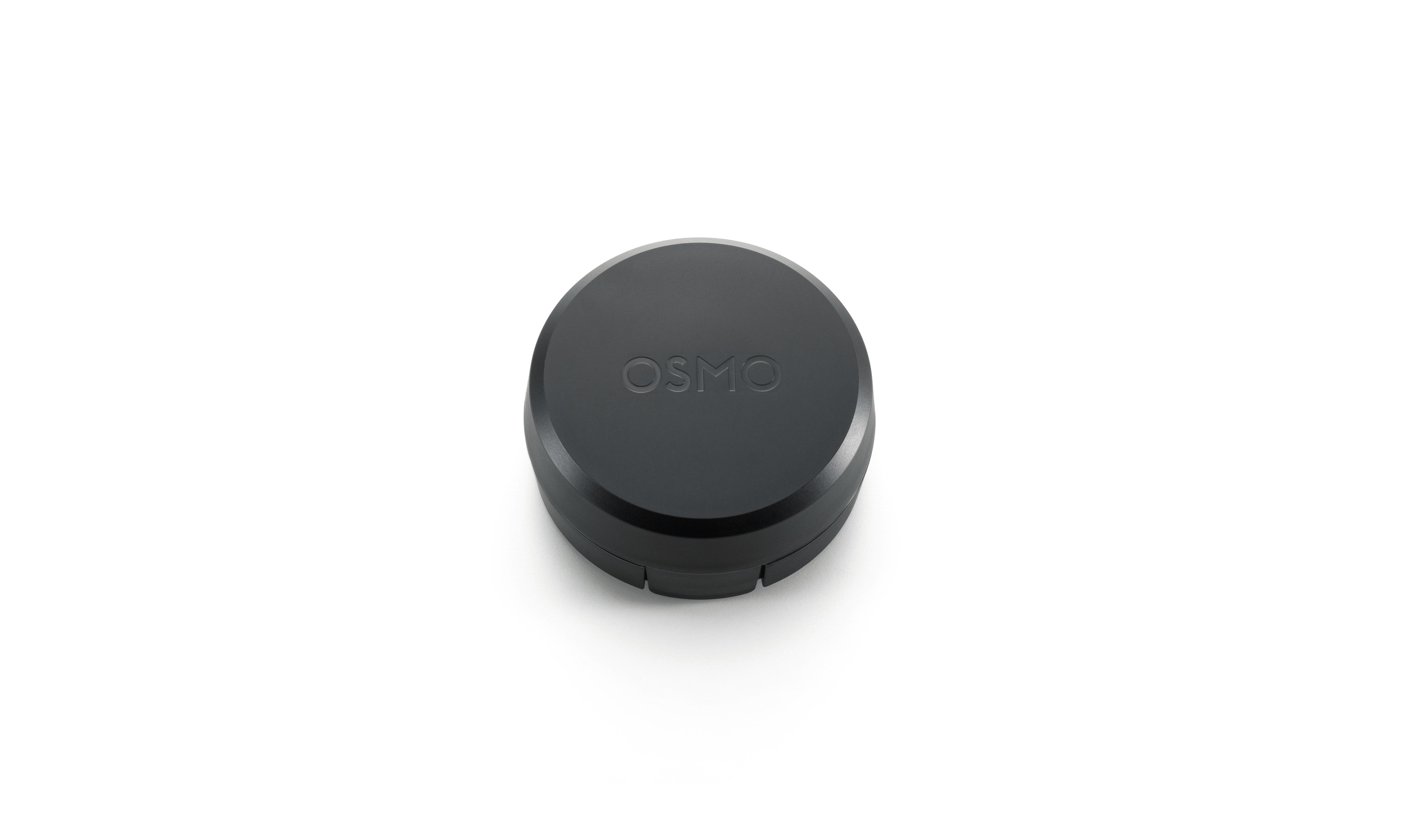 Ein schwarzes Osmo-Gerät, kreisförmig mit Markennamen oben, liegt auf weißem Hintergrund. Das Gerät hat ein zweiteiliges Design.