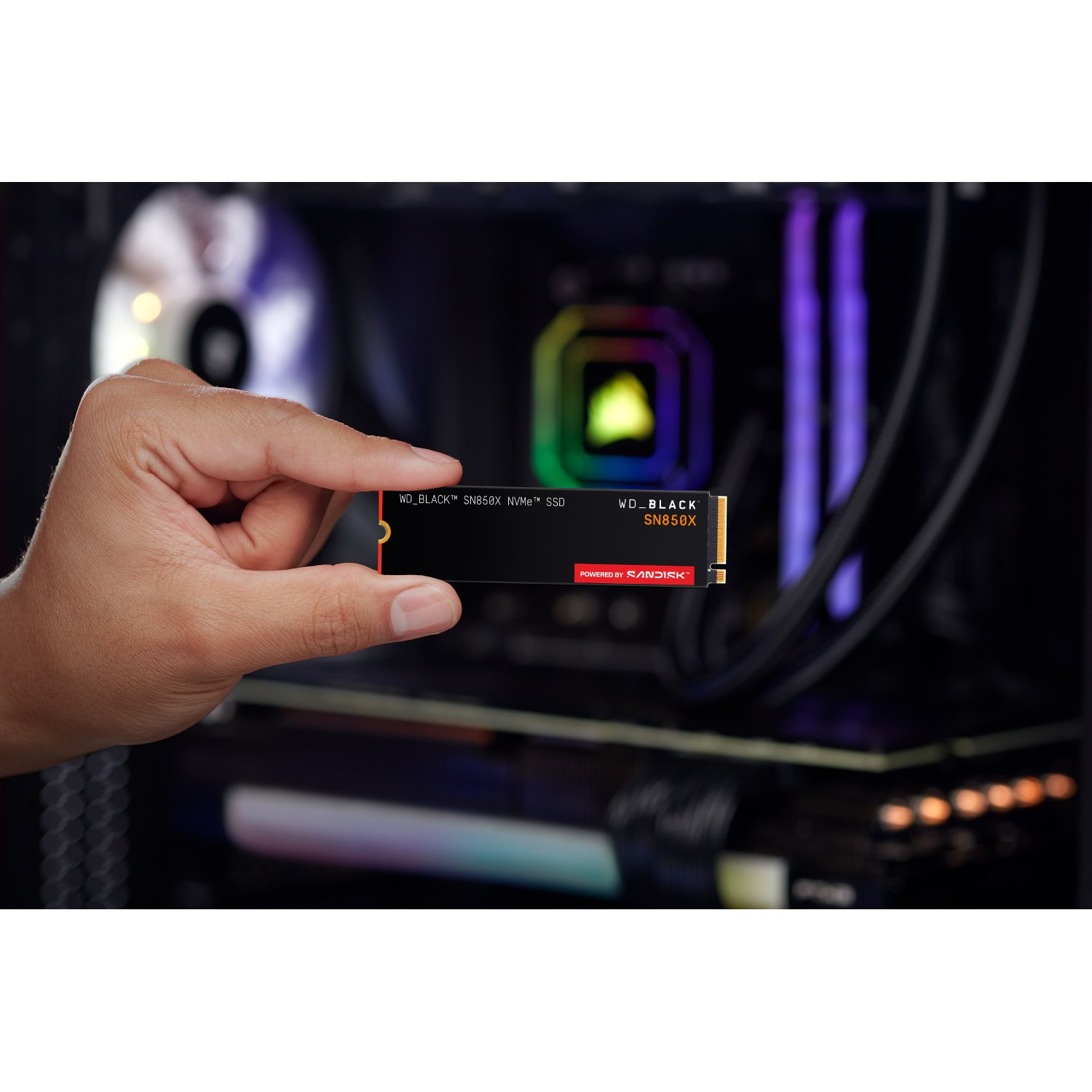 Una mano sosteniendo un SSD NVMe WD_BLACK SN850X negro. El fondo muestra componentes de computadora con luces coloridas.