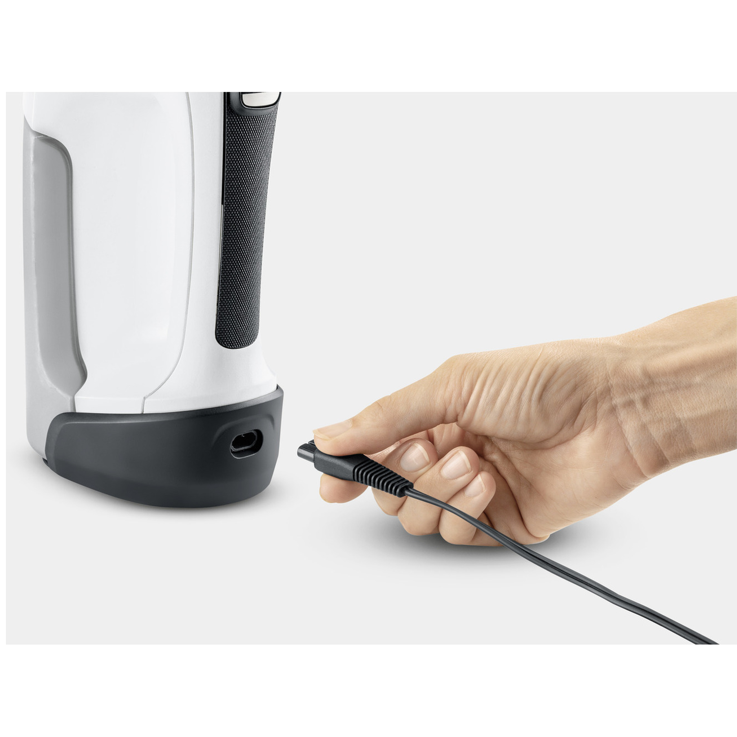 A hand holding a black cable is about to plug it into a white and black device. The background is white.