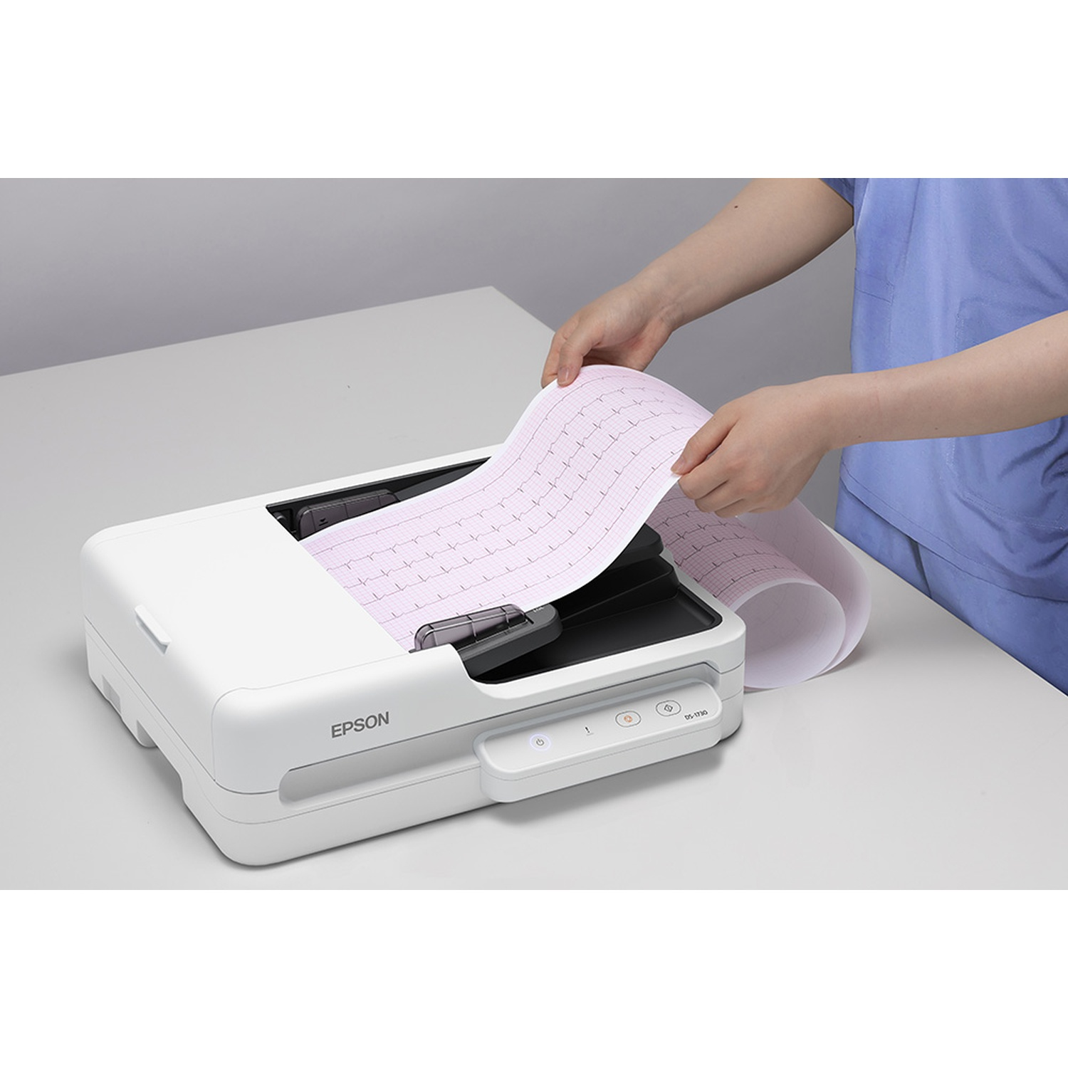 Una persona tiene in mano una stampa ECG arrotolata sopra una stampante Epson. La stampante è bianca e la stampa ha linee a griglia rosa.