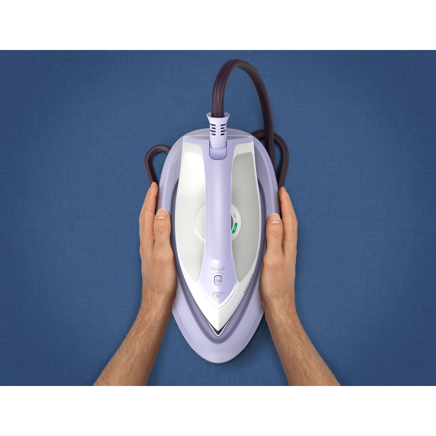 Hands holding a light purple iron on a blue textured surface. A dark cord extends from the iron.