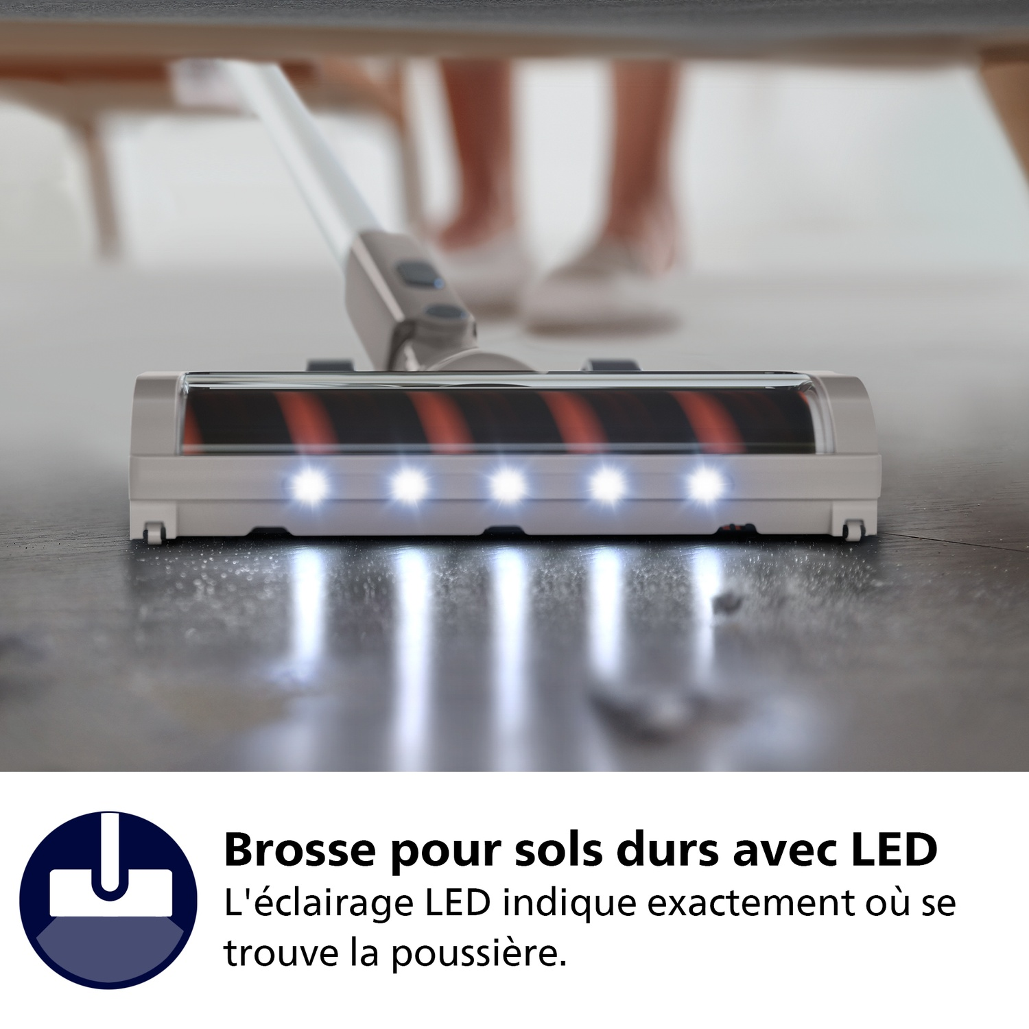 Une tête d'aspirateur avec des lumières LED nettoie le sol. Les jambes et les pieds d'une personne sont visibles en arrière-plan.