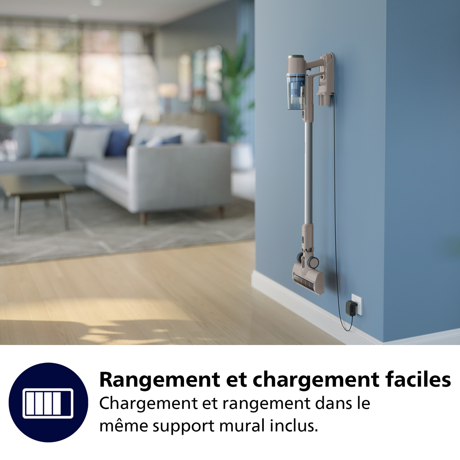 Aspirateur sans fil monté sur un mur bleu. Salon en arrière-plan. L'aspirateur est en charge. Texte : Rangement et chargement faciles.