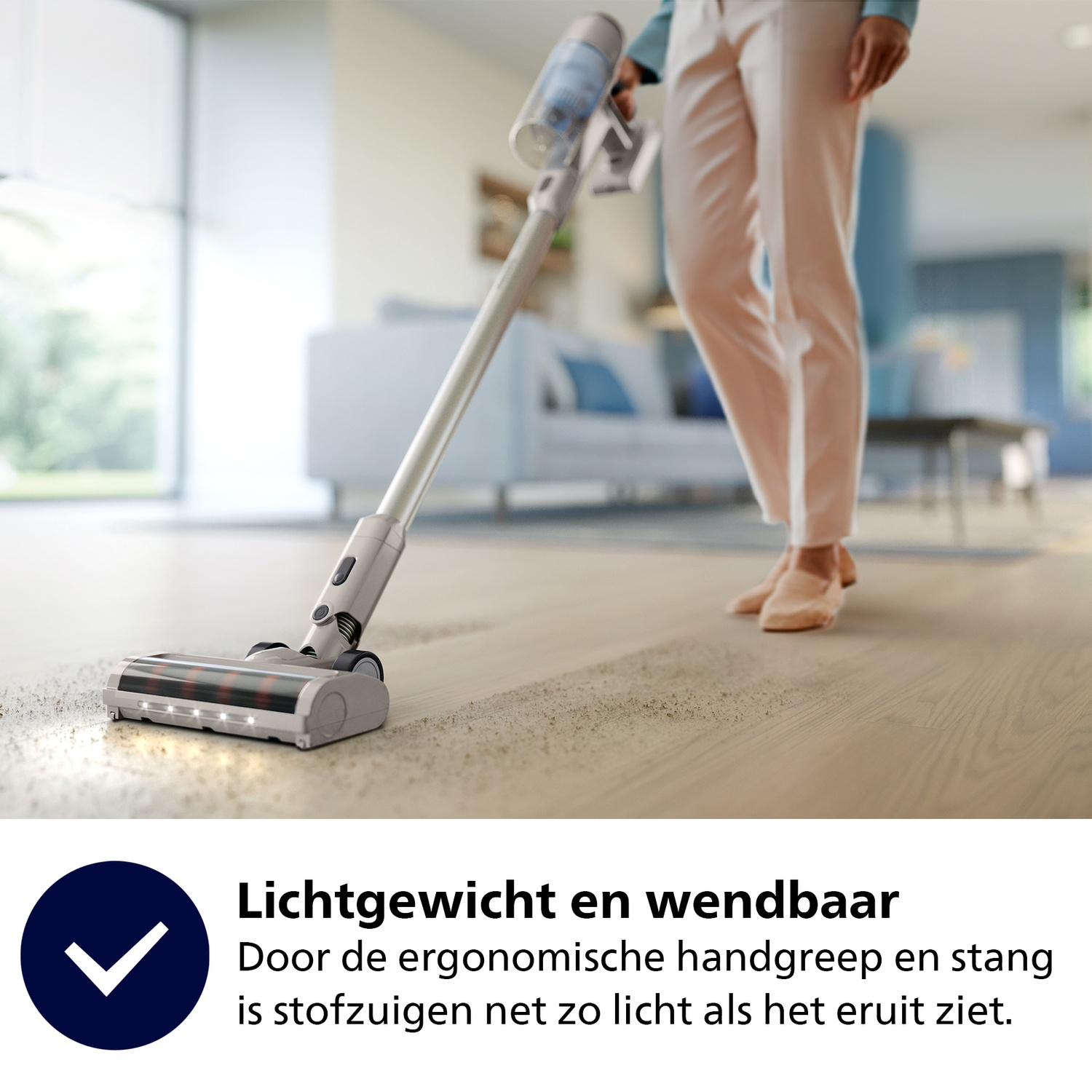 Een persoon stofzuigt een houten vloer met een draadloze stofzuiger. De achtergrond toont een woonkamer met een bank.