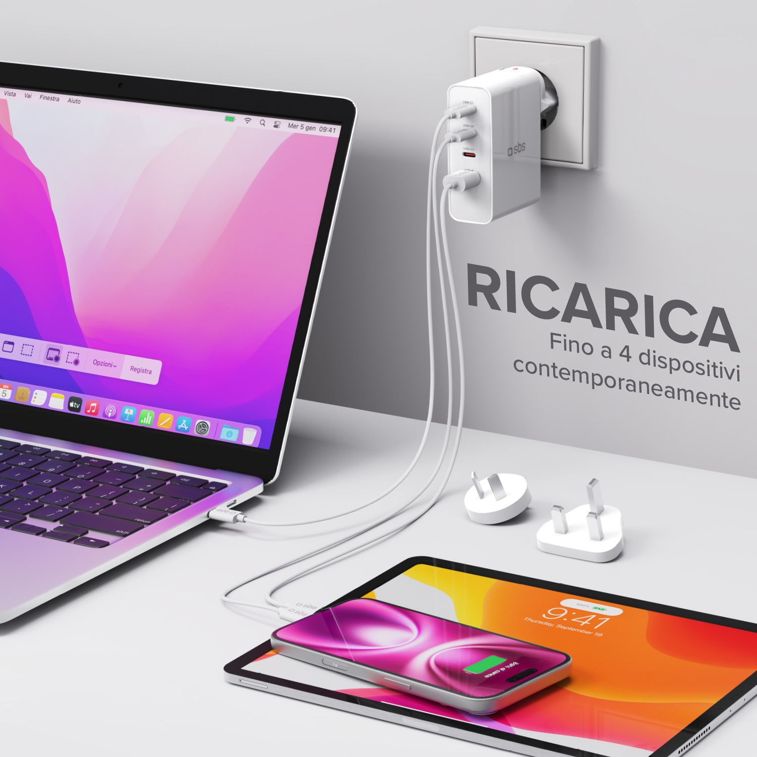 Laptop, tablet e telefono in carica con un caricatore bianco. Il telefono e il tablet sono su un tavolo. Lo sfondo è bianco.