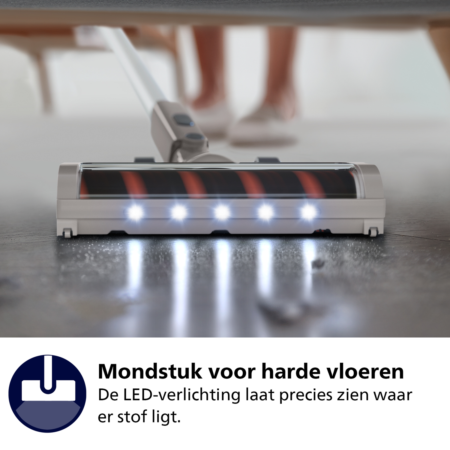 Close-up of a vacuum cleaner head with LED lights illuminating a floor. A person's legs are blurred in the background.