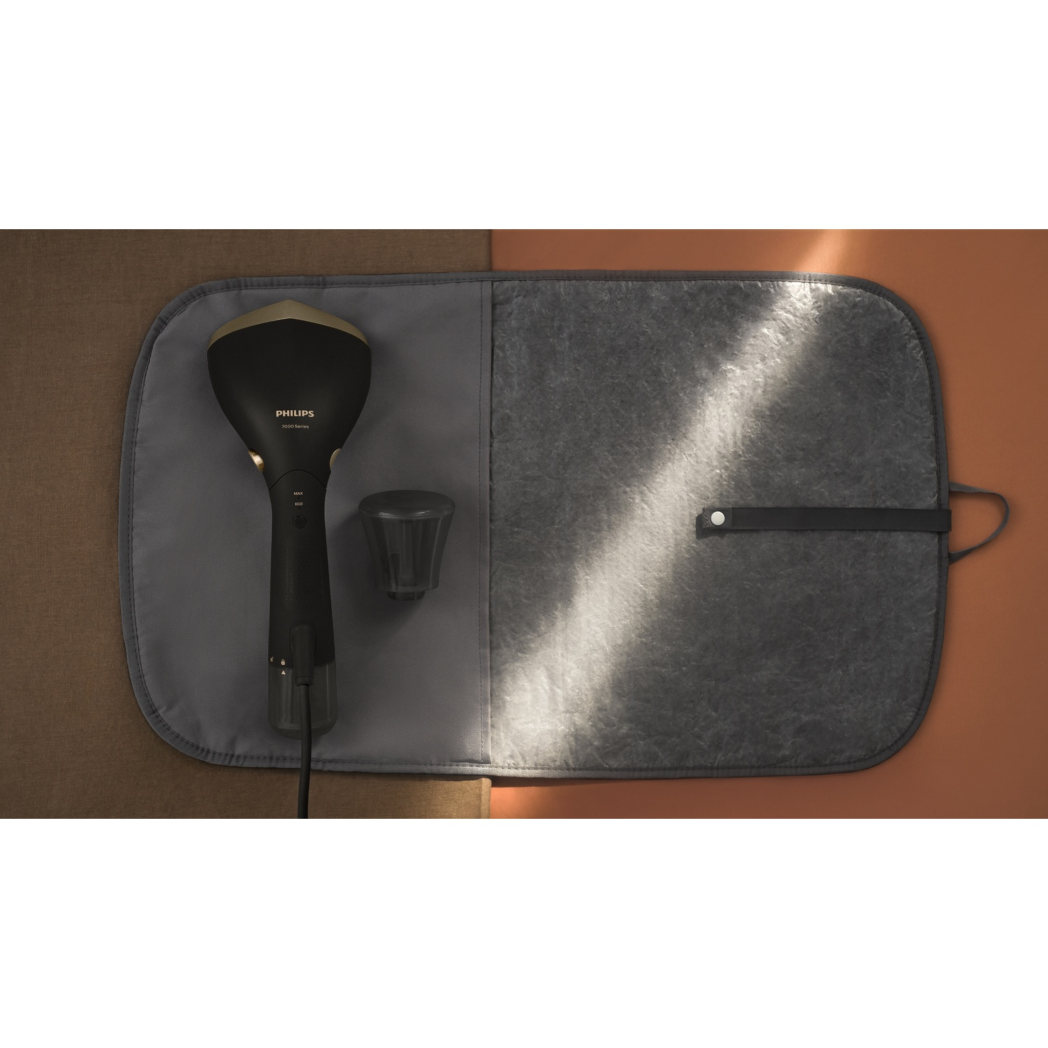 Un défroisseur Philips noir avec accessoires sur une planche à repasser grise. Le fond est marron.